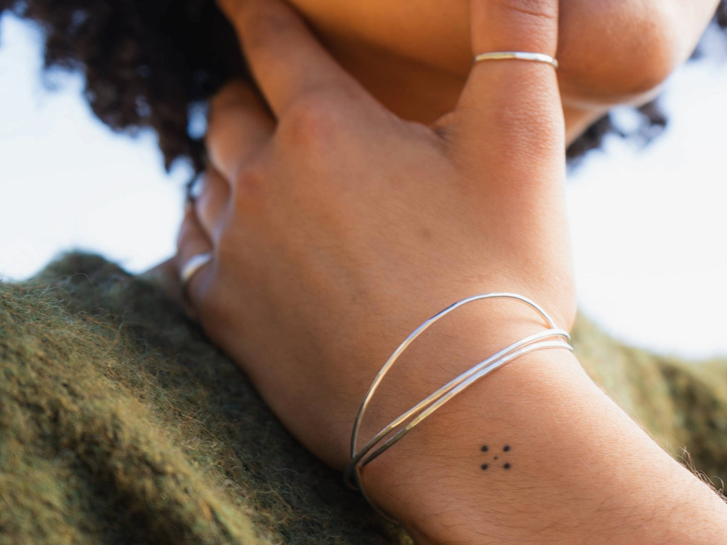 Close up of a woman in a green jumper wearing three textured silver bangles
