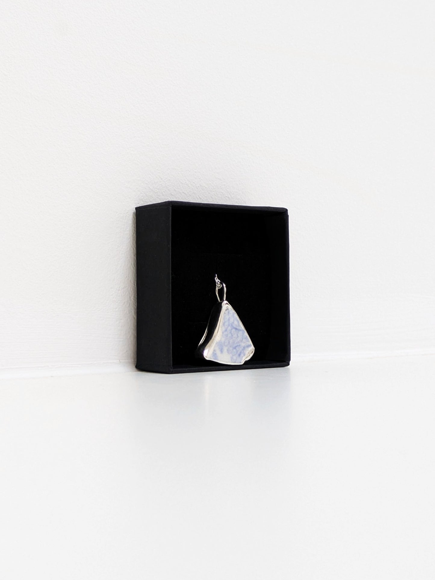 Close up angle of a black jewellery display box with a blue floral sea pottery pendant on a white background