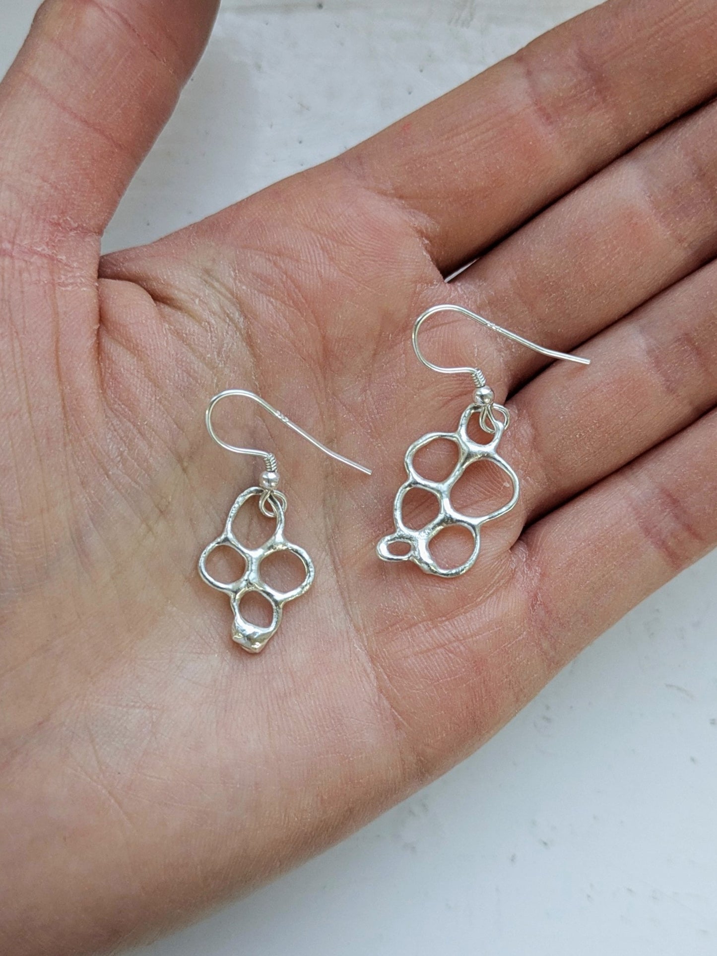 Organic shaped silver drop earrings in palm of a hand