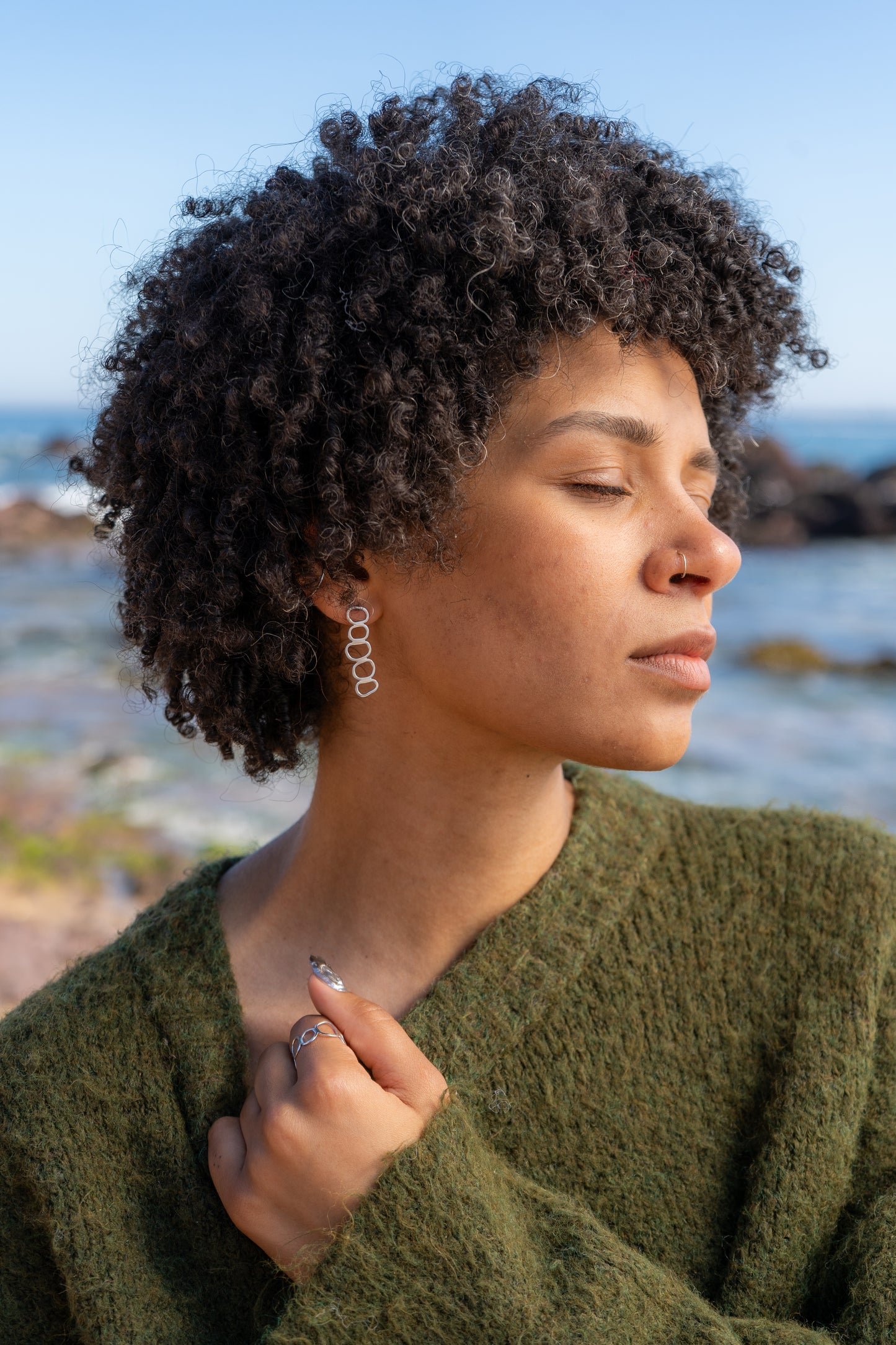 Woman with natural hair wearing a green jumper and cairn jewellery by the sea
