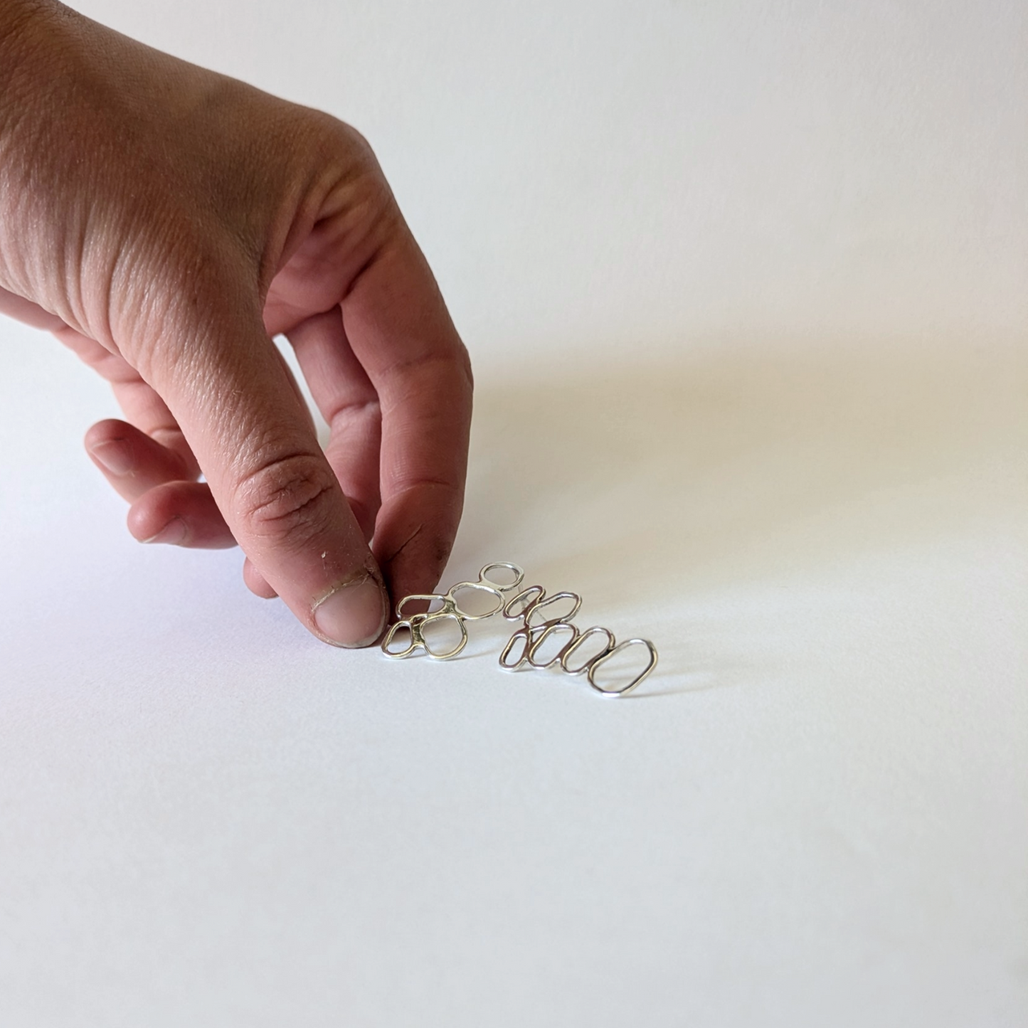 Hand holding silver clustered pebble earrings on white background