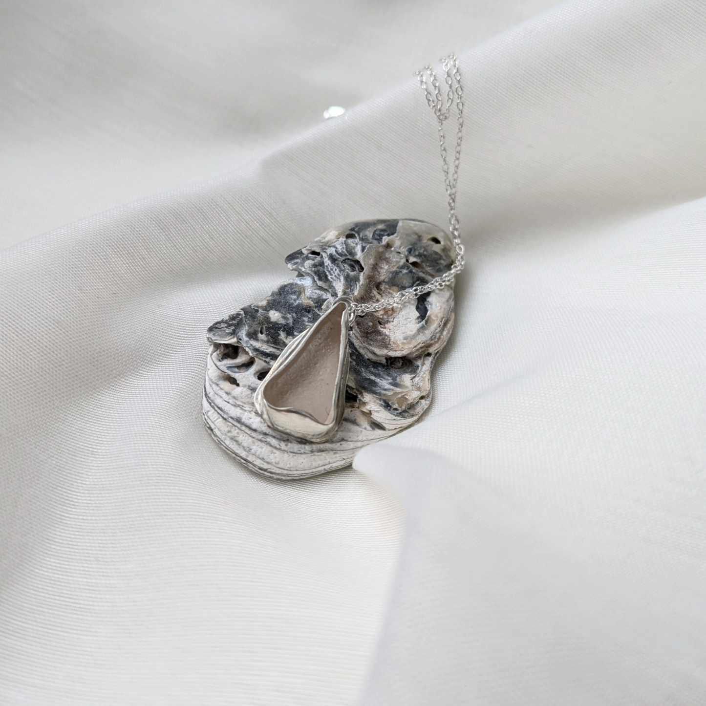 Sea glass necklace on oyster shell with white silk background