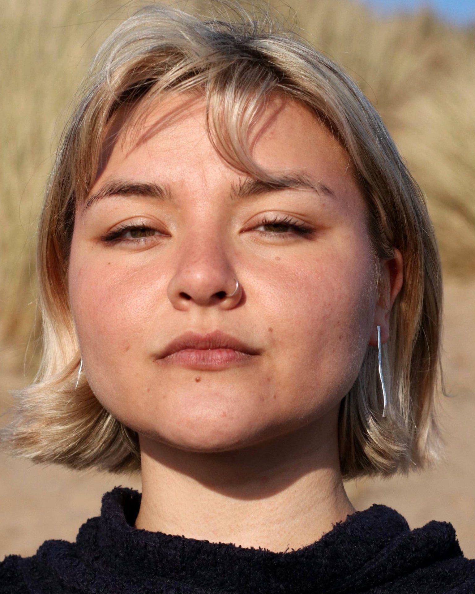 Woman wearing hammered line earrings on beach with blue sky in background