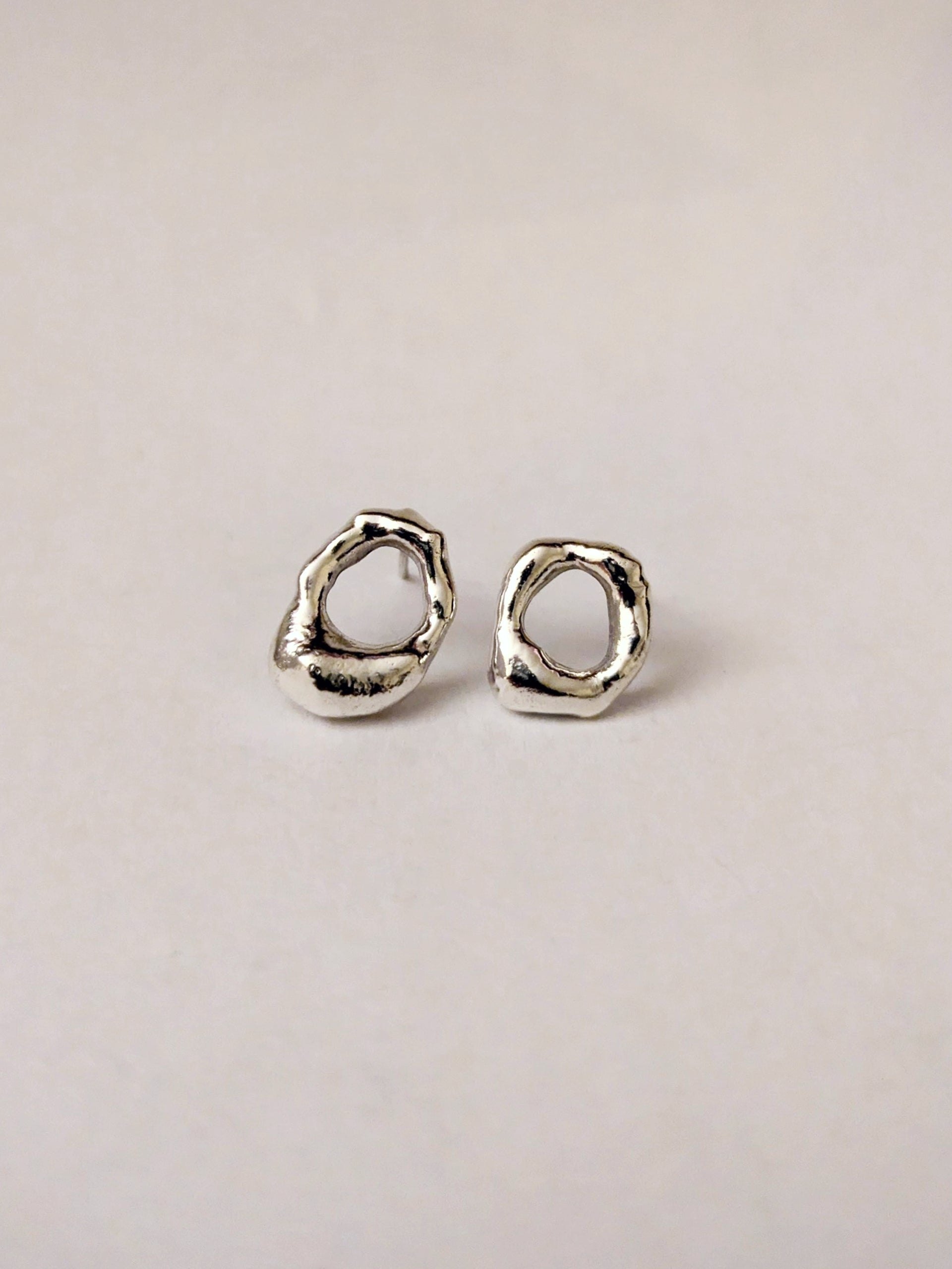 Pair of silver mini molten earrings on a light beige background