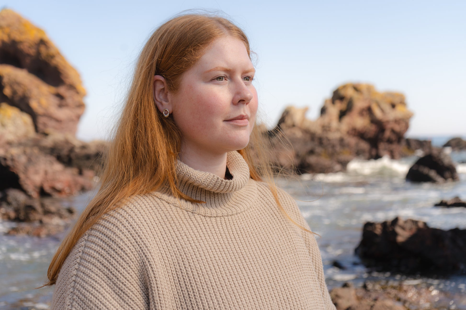 Woman with red hair standing on a rocky beach wearing mini molten studs