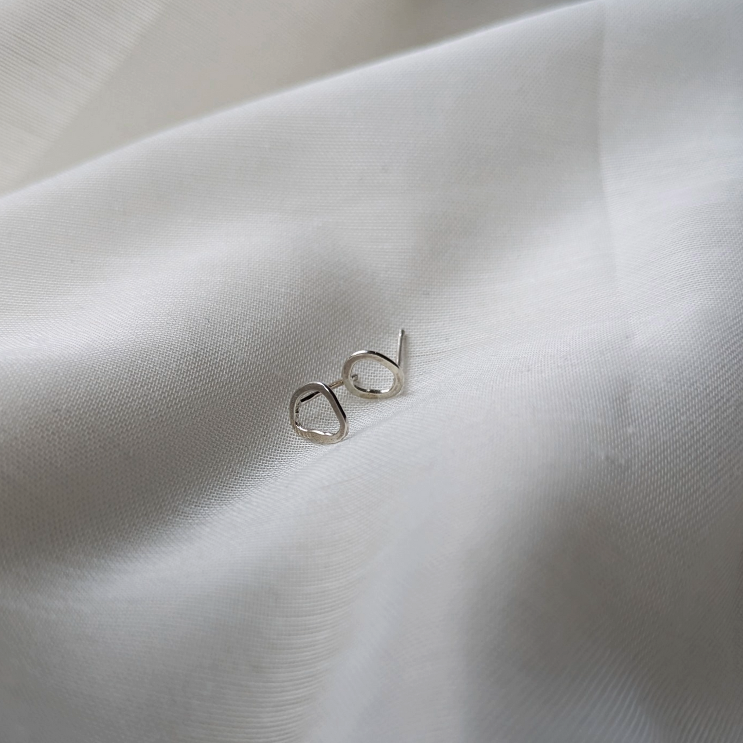 Silver pebble stud earrings on white silk
