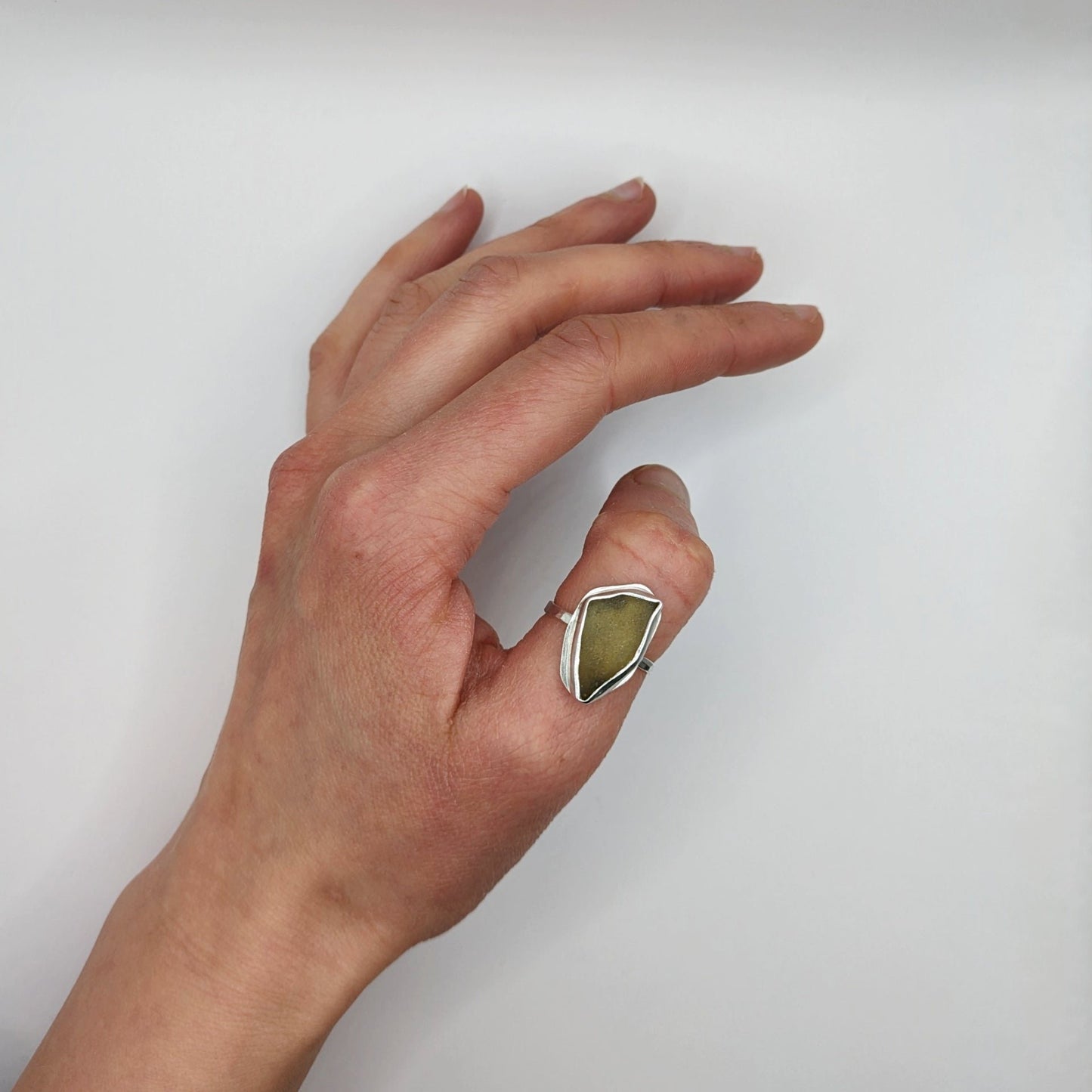 Green sea glass silver ring on thumb with white background