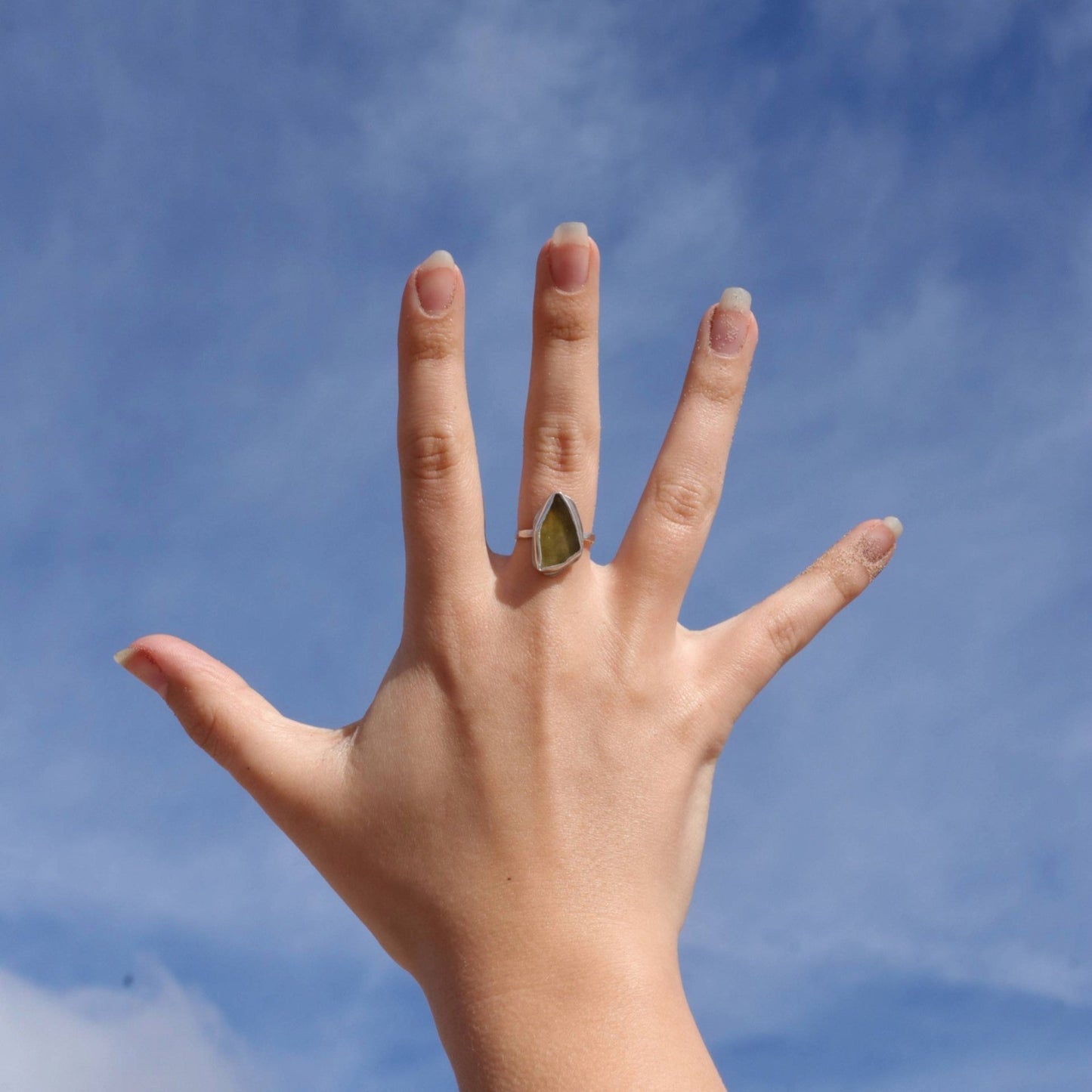 Green sea glass on a silver ring on a hand with sky in background
