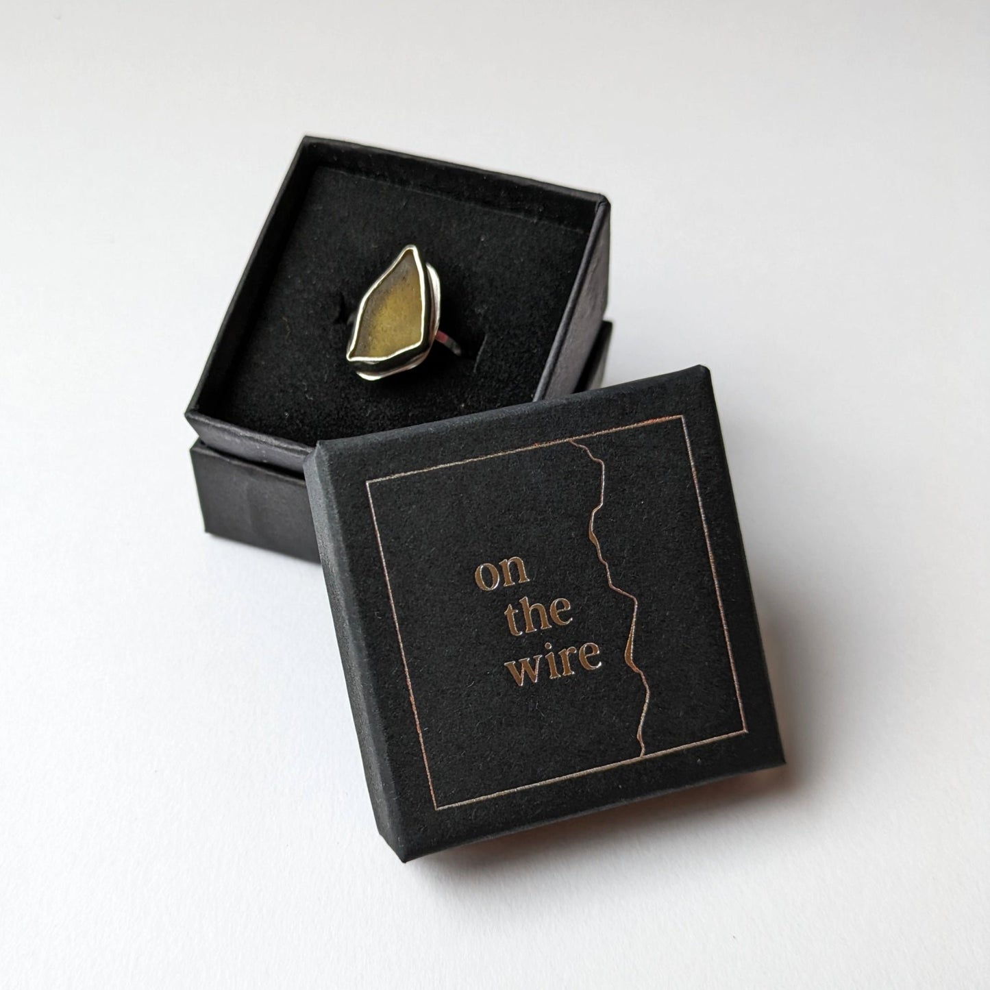 Green sea glass on a silver ring in a branded gift box on white background