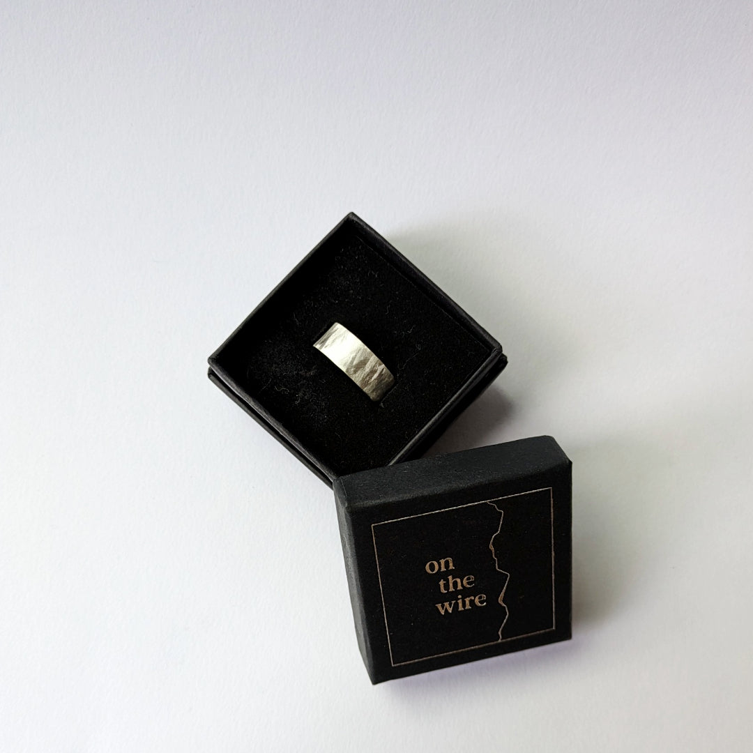 Small feather textured silver ring in branded box on white background