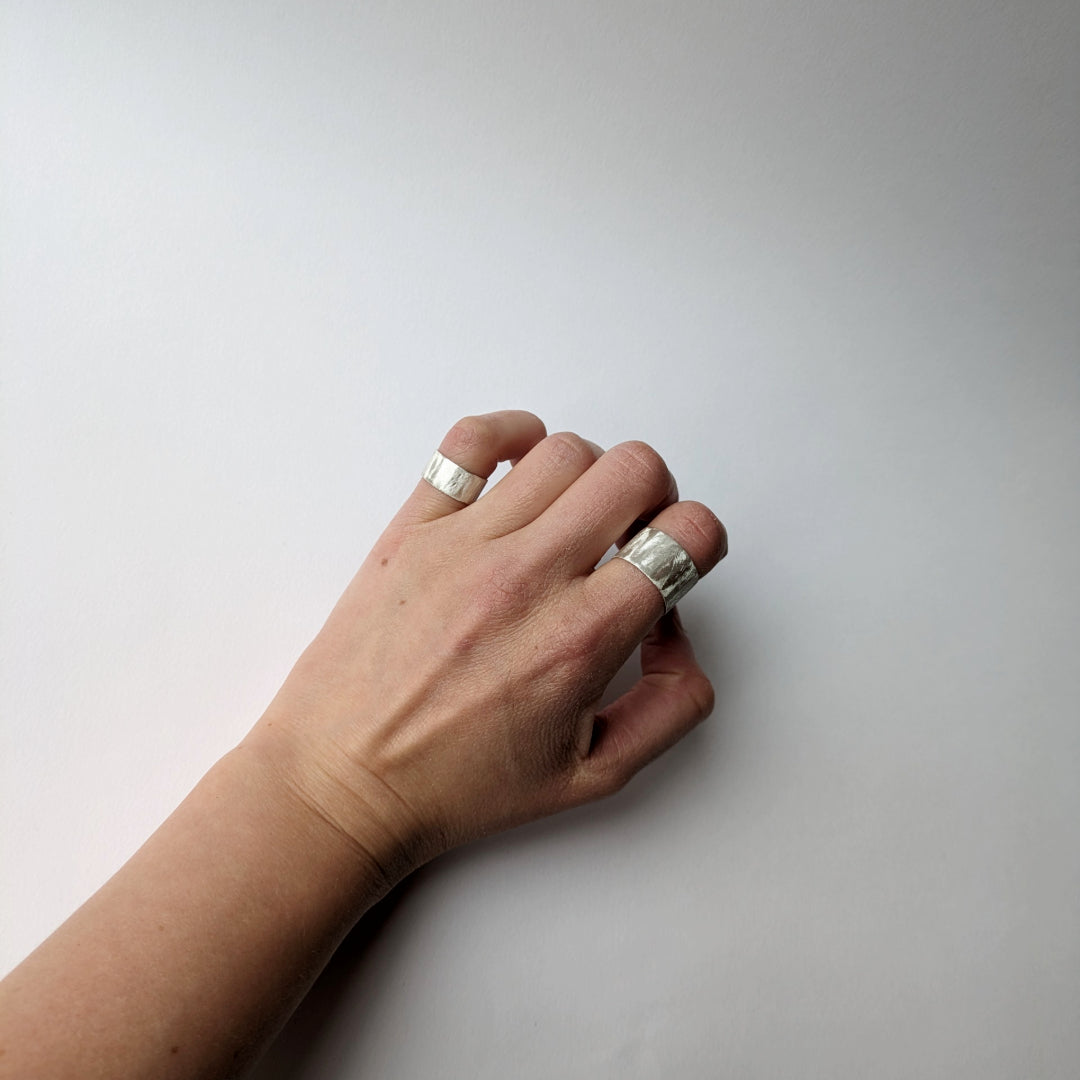Feather textured silver rings on pinky and forefinger white background