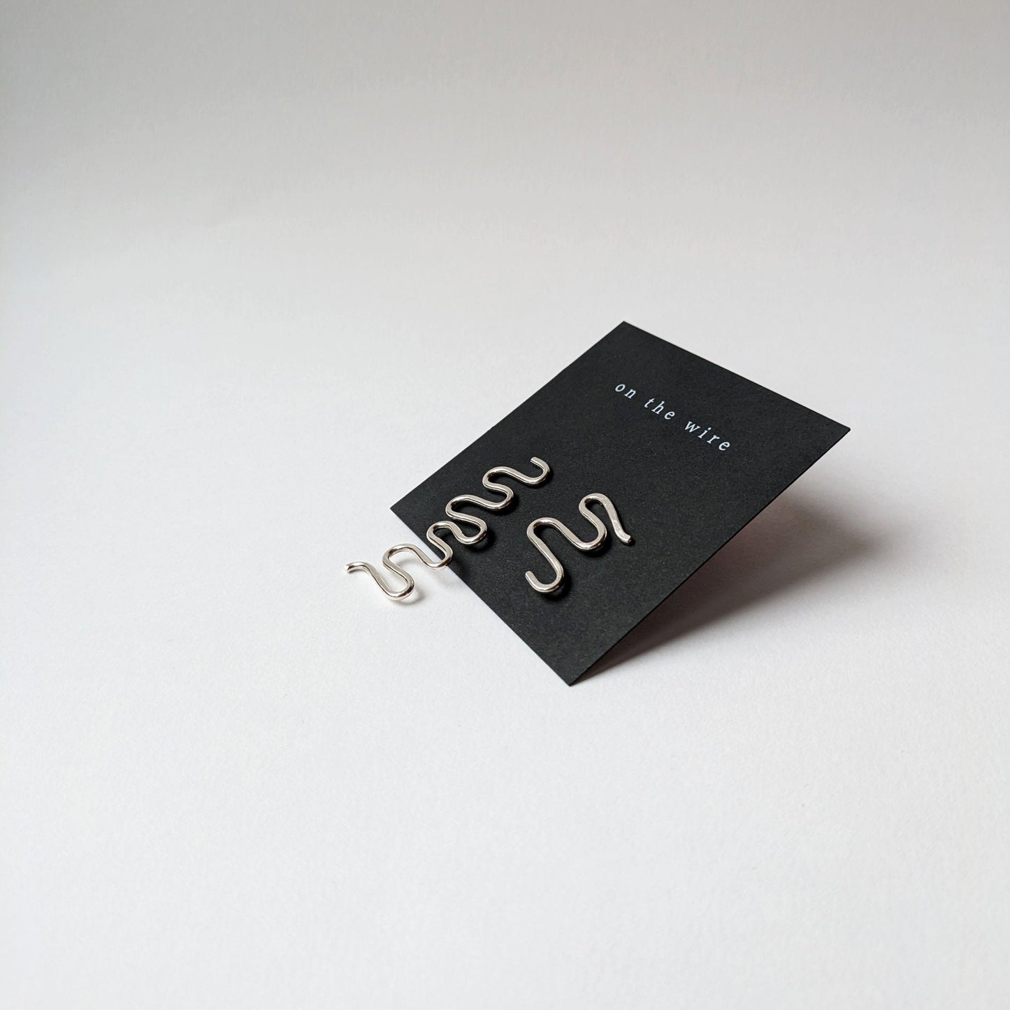 Asymmetric silver wiggle studs on black branded earring card