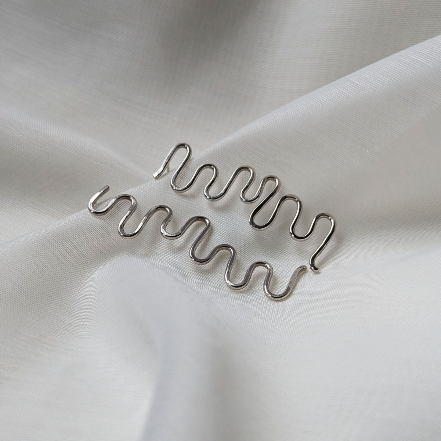 Silver wiggle earrings on white silk
