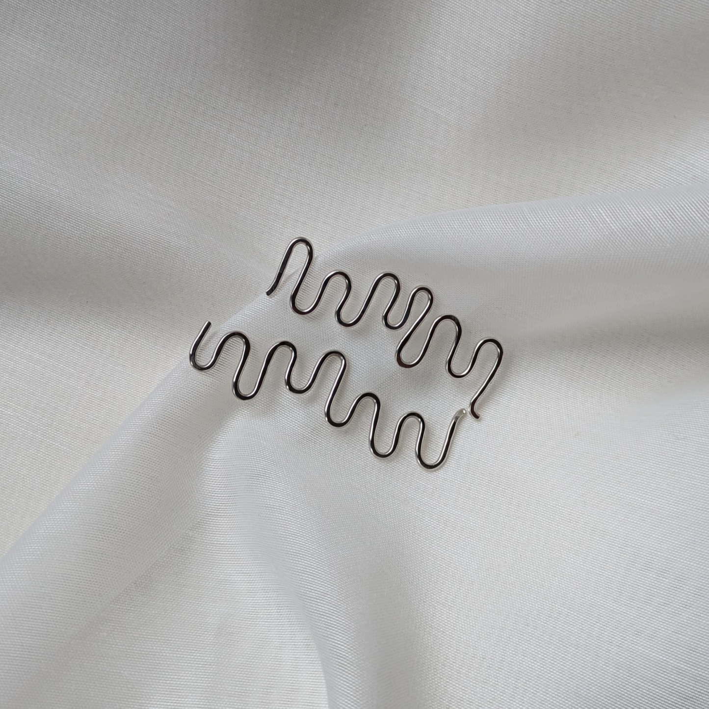 Silver wiggle earrings on white silk