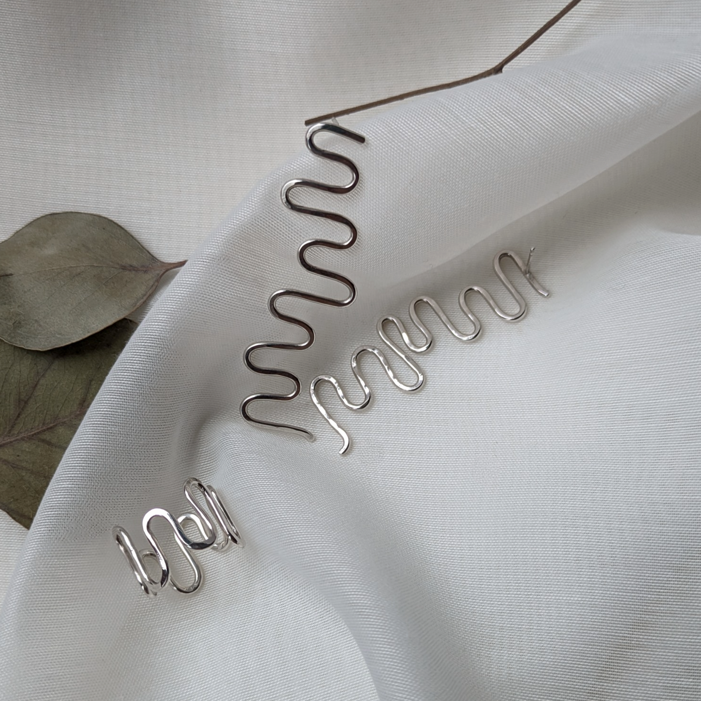 Silver wiggle ring and wiggle earrings on white silk with eucalyptus leaves
