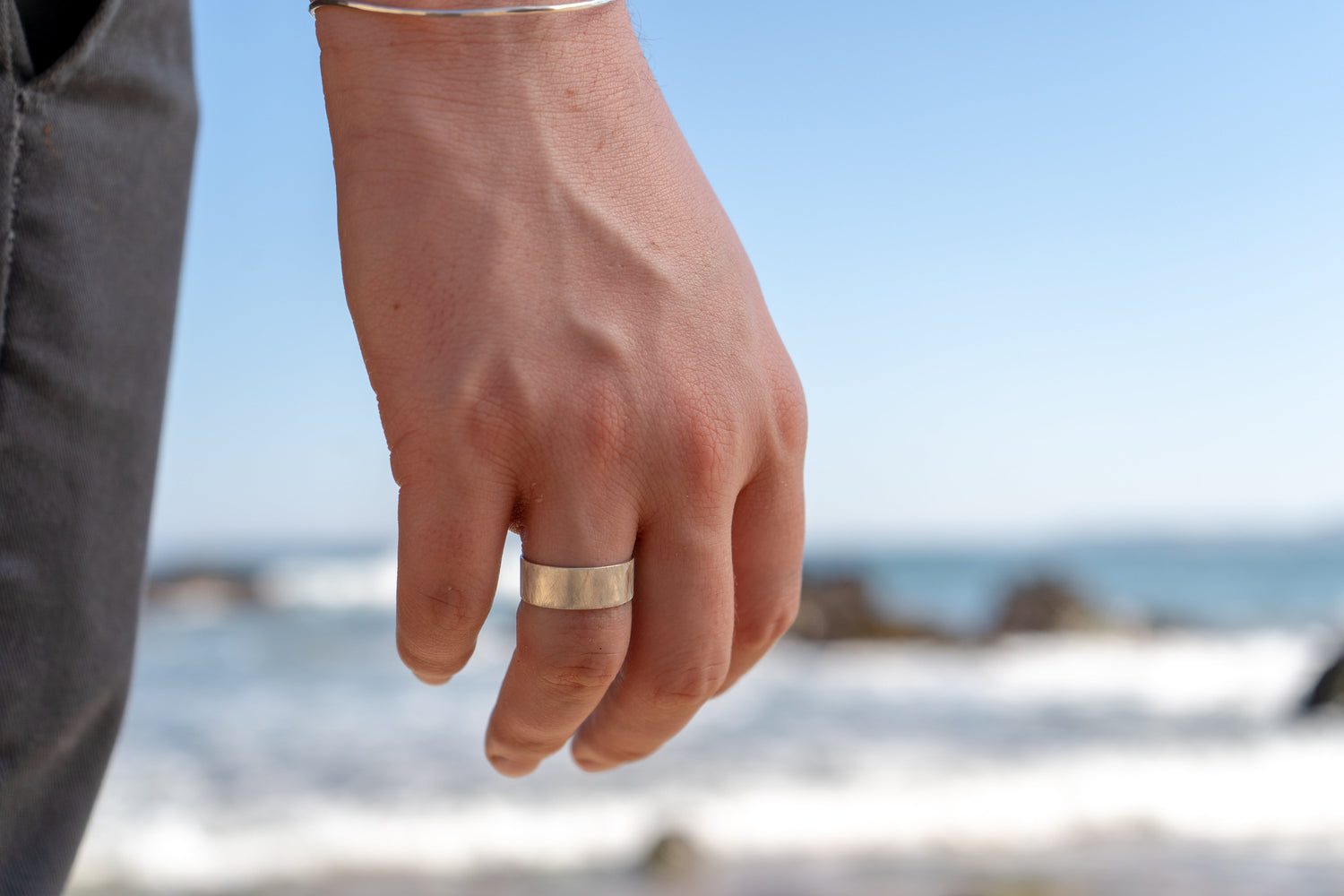 Close up of a silver ring on a man's hand with the sea in the background