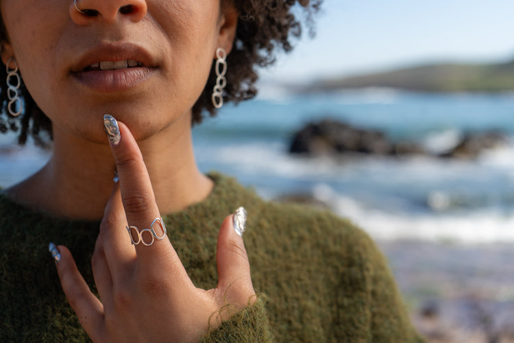 A woman in a green jumper wears silver stacked pebble earrings and a silver stacked pebble ring