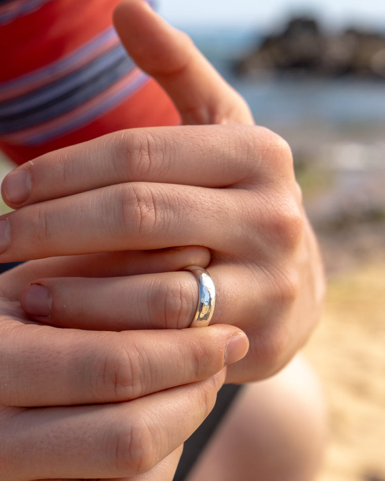 Close up of a man wearing a red striped t-shirt holding his hand with a mottled silver ring on one finger