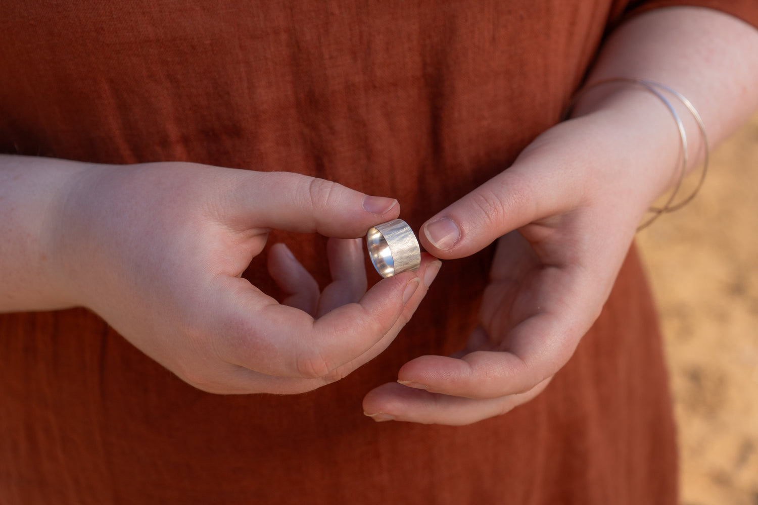 Close up of a woman wearing an orange linen dress holding a chunky recycled silver ring 
