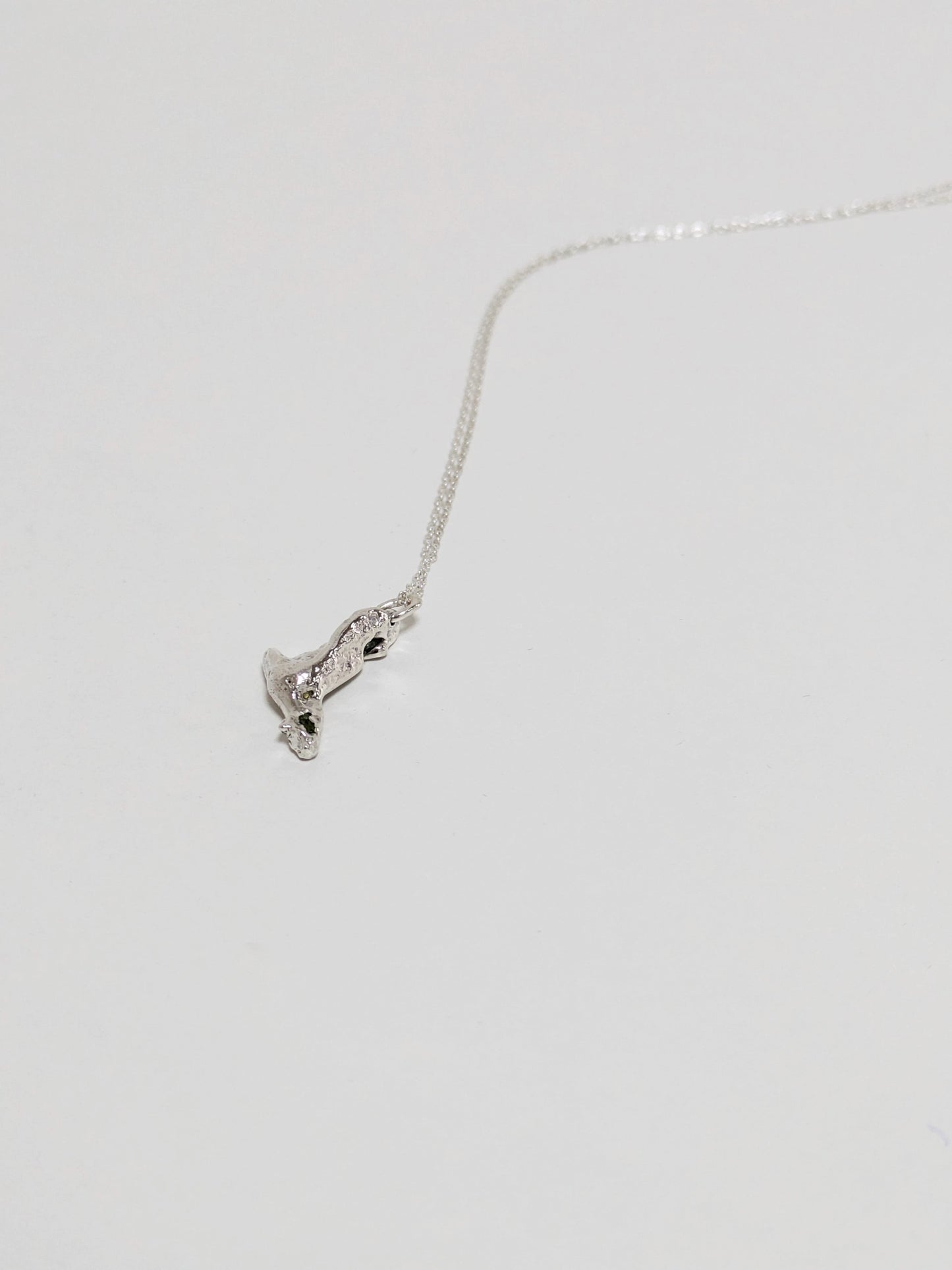 A silver pendant embedded green sea glass shards lying on a white background