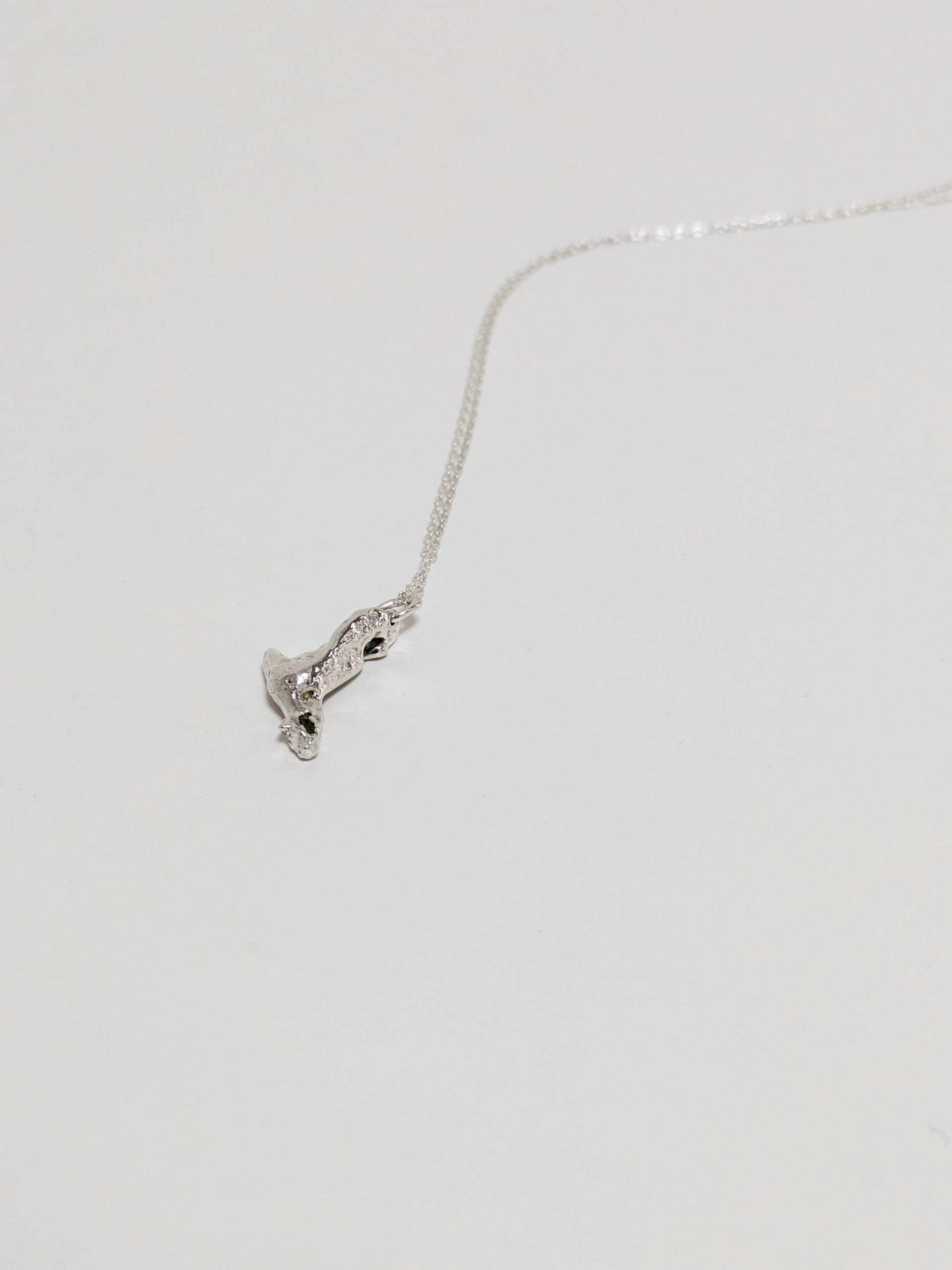 A silver pendant embedded green sea glass shards lying on a white background