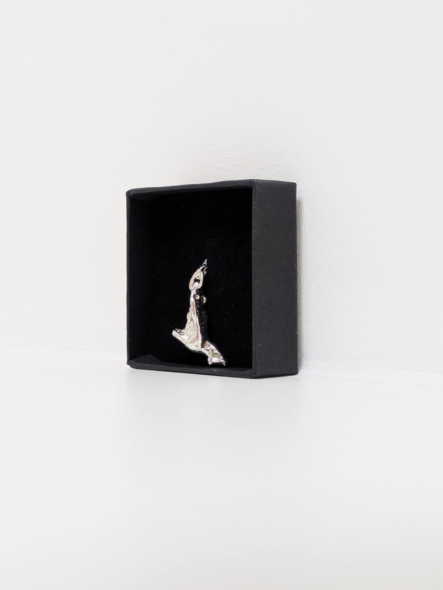 Side angle of a silver pendant embedded green sea glass shards in a black jewellery box on a white background