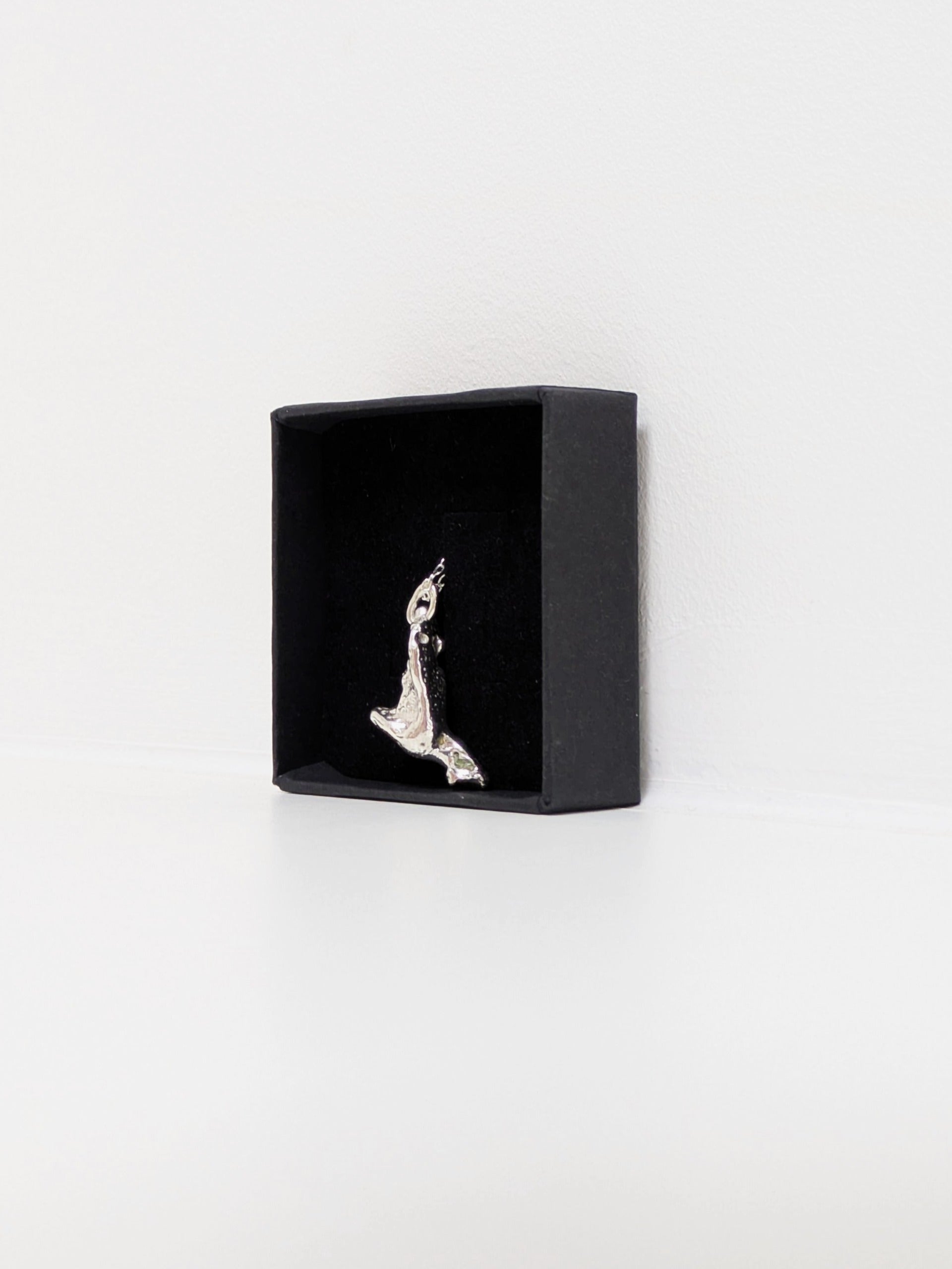 Side angle of a silver pendant embedded green sea glass shards in a black jewellery box on a white background