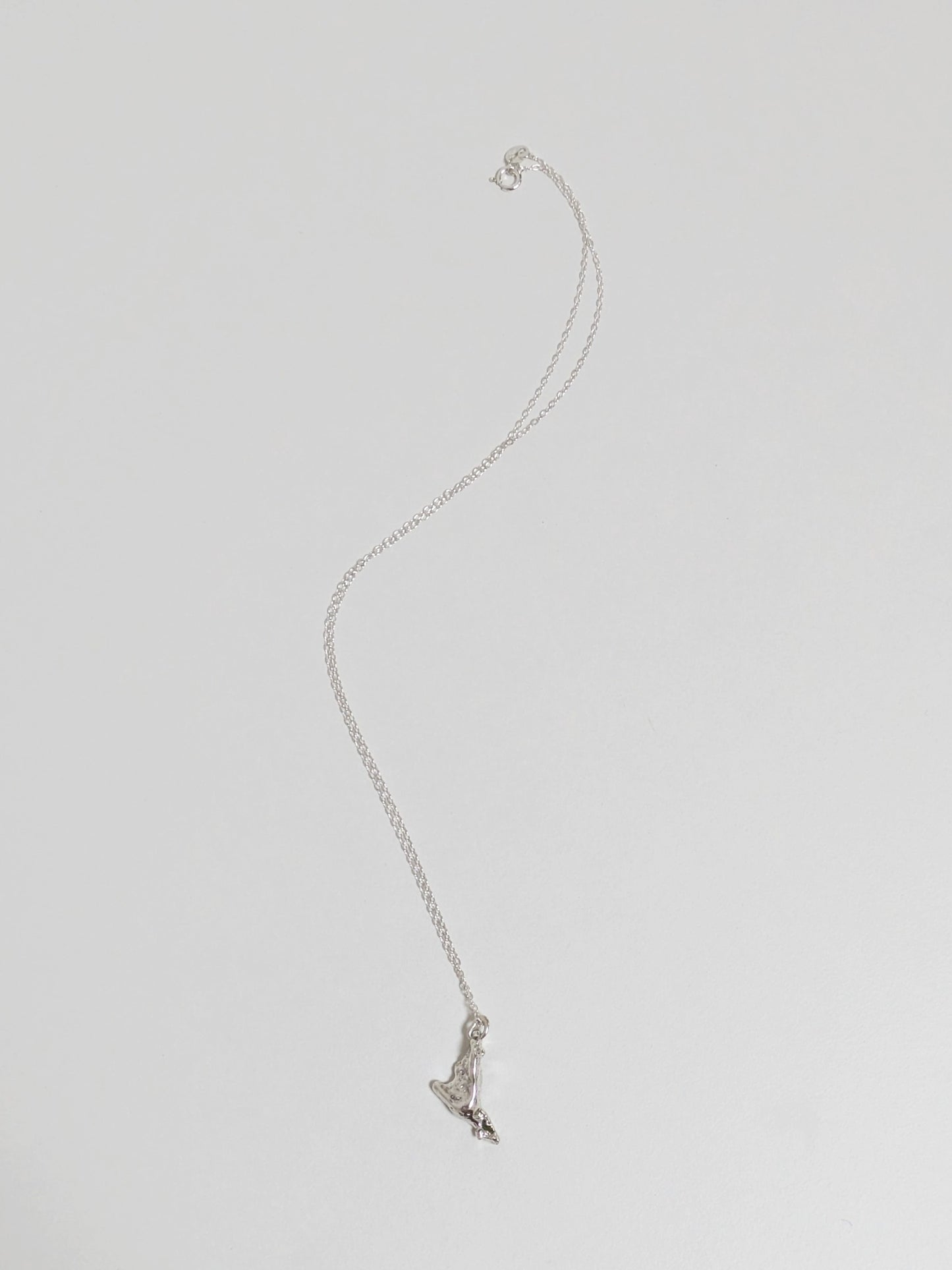 A silver pendant embedded with green sea glass shards on a silver chain lying on a white background