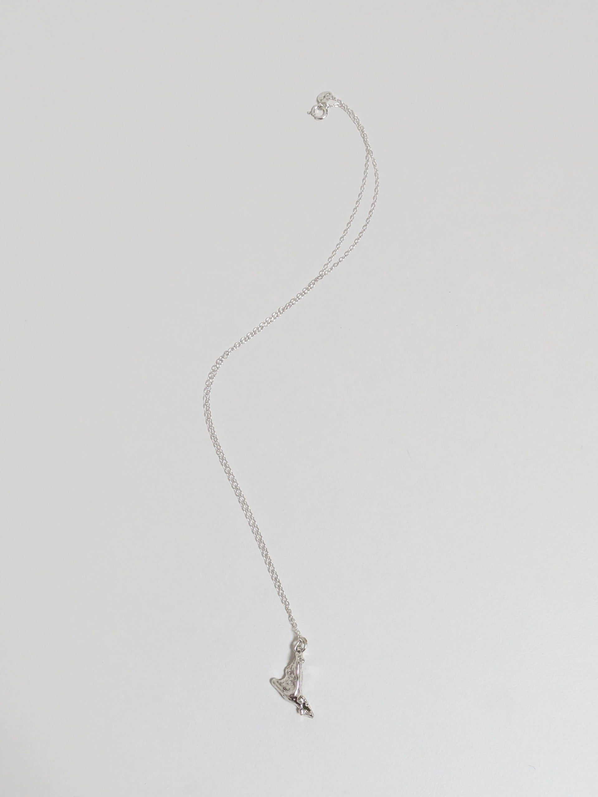 A silver pendant embedded with green sea glass shards on a silver chain lying on a white background