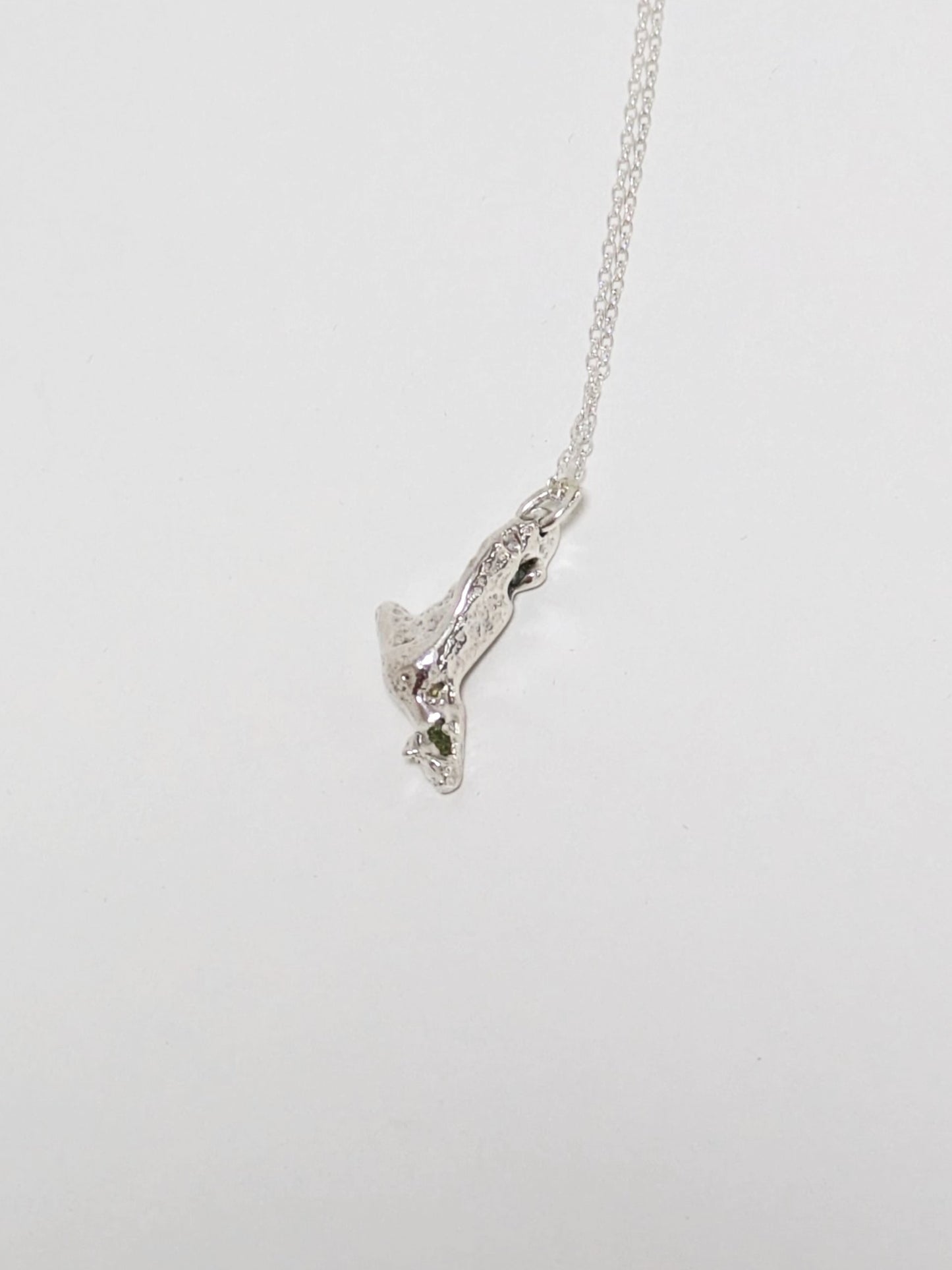 Close up of a silver pendant embedded green sea glass shards on a light grey background