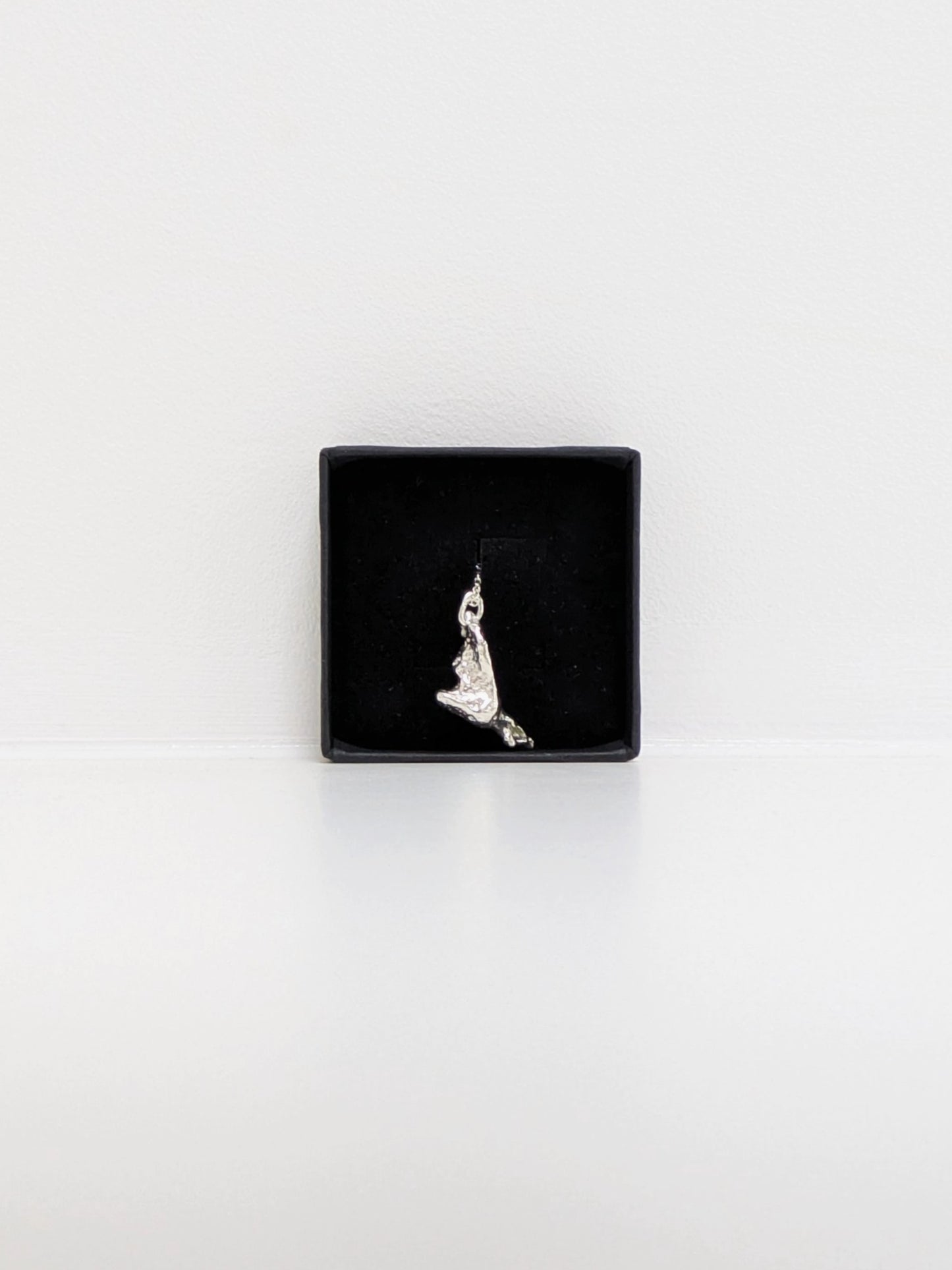 A silver pendant embedded with green sea glass shards in a black jewellery box on a white background