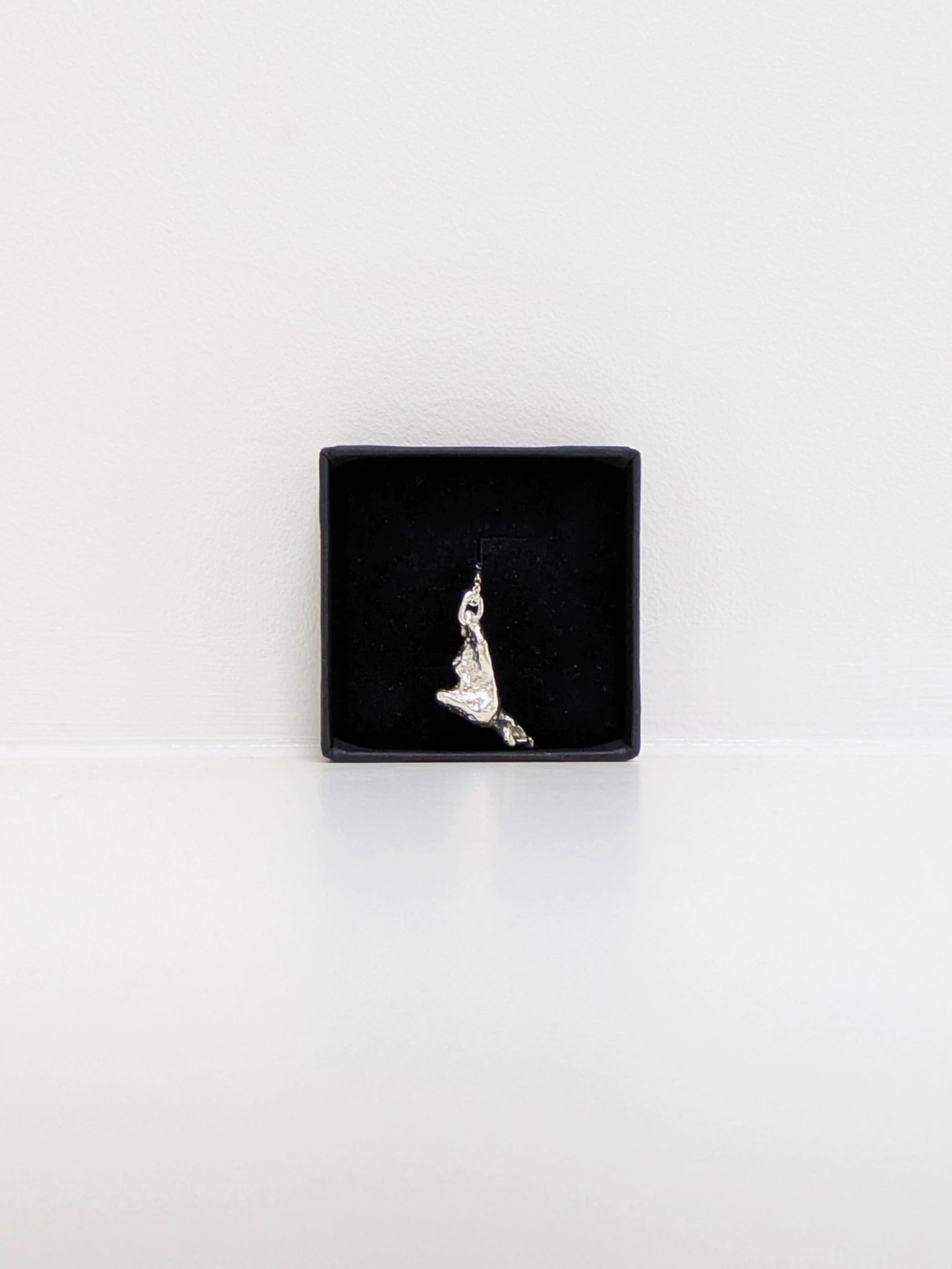 A silver pendant embedded with green sea glass shards in a black jewellery box on a white background