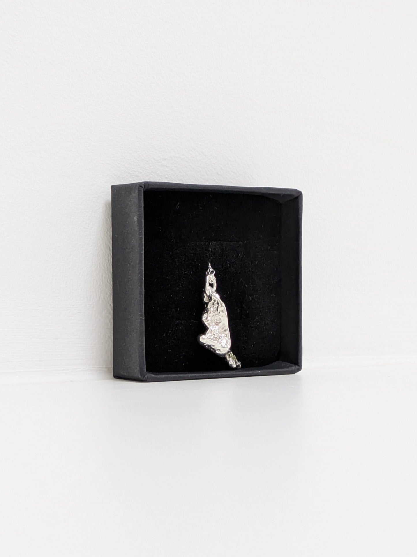 Side angle of a silver pendant embedded green sea glass shards in a black jewellery box on a white background