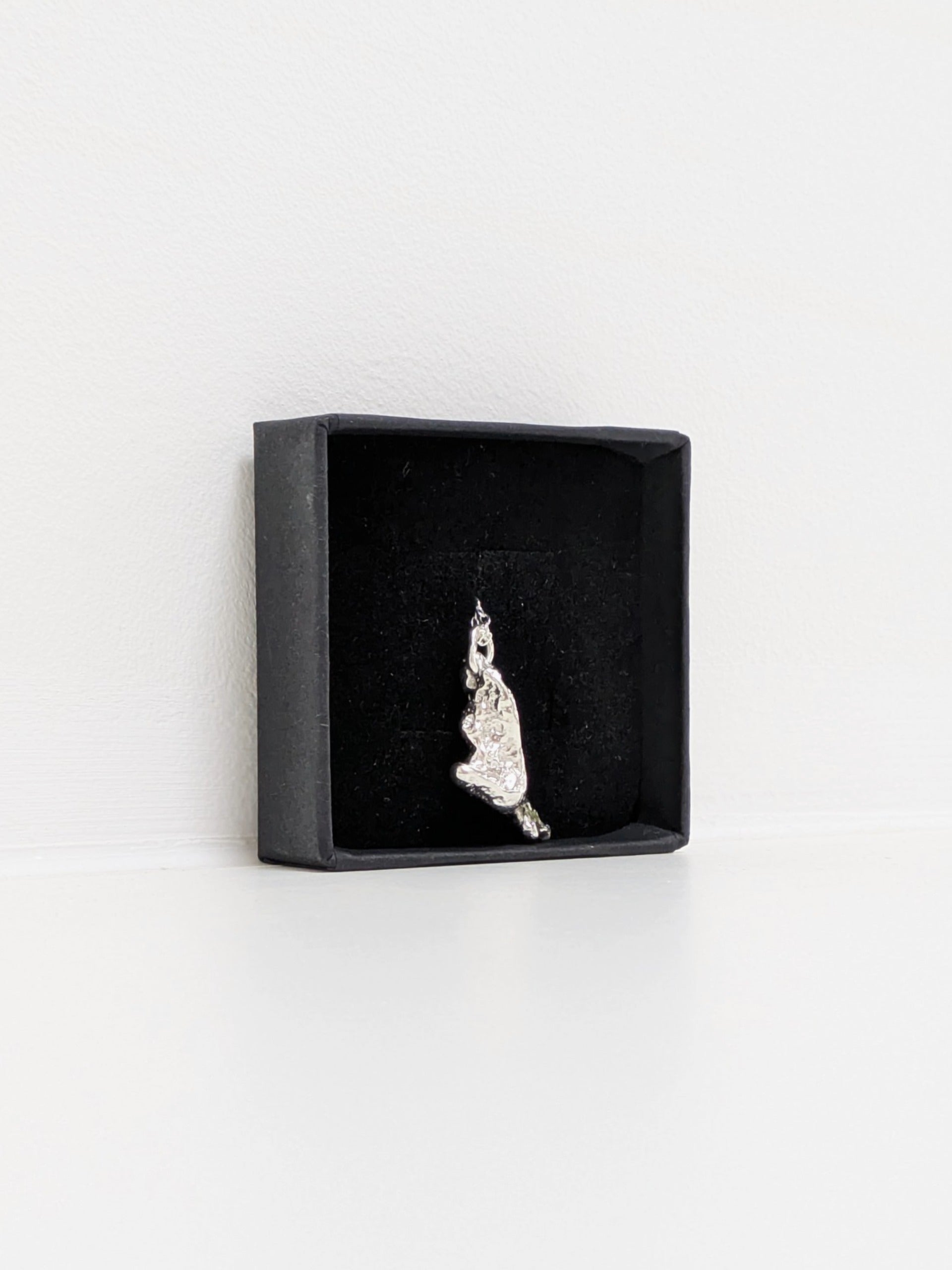 Side angle of a silver pendant embedded green sea glass shards in a black jewellery box on a white background