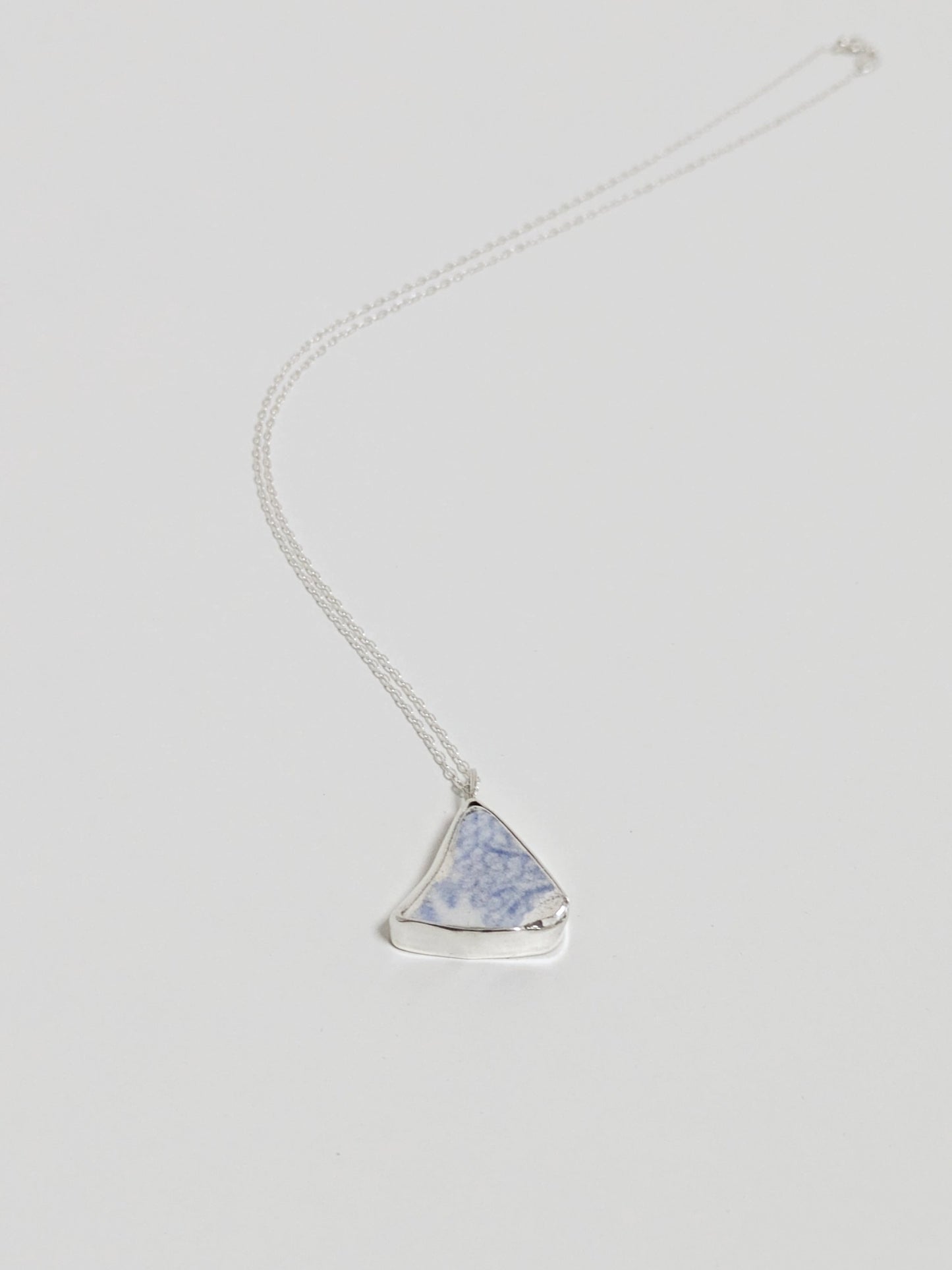 Necklace with a triangular blue floral sea pottery pendant on a light gray background