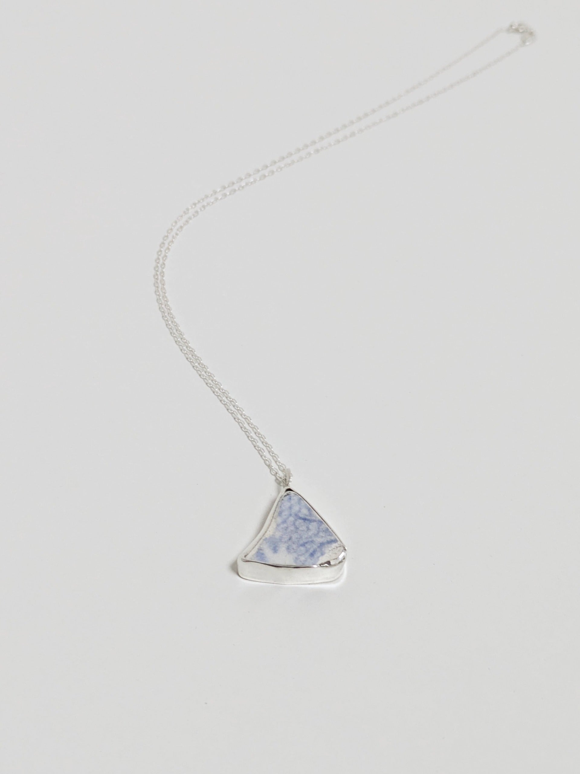 Necklace with a triangular blue floral sea pottery pendant on a light gray background