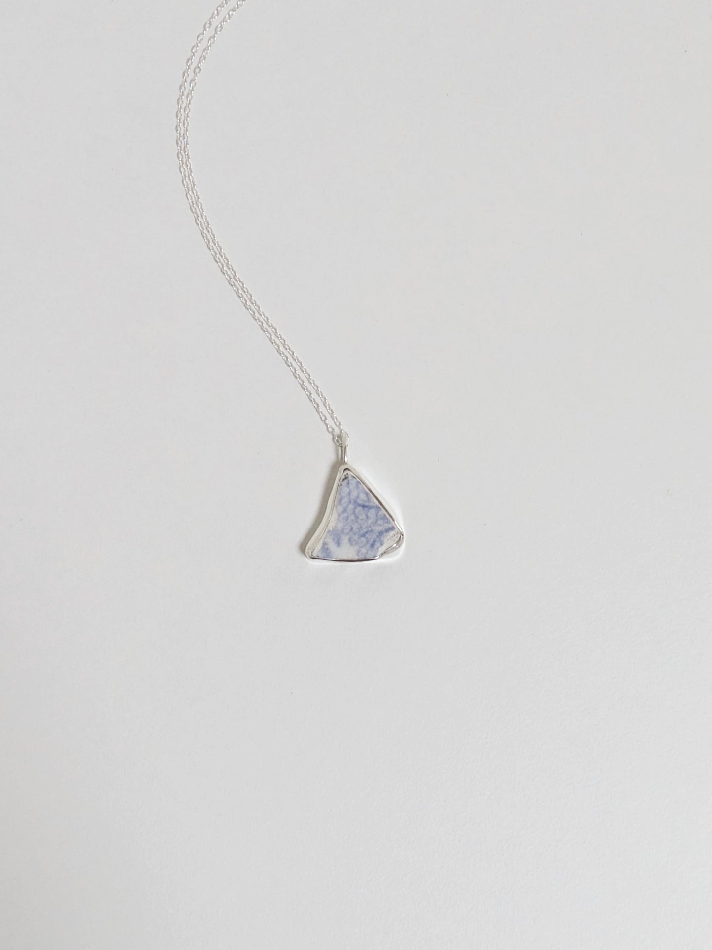 Silver necklace with a triangular blue floral sea pottery pendant on a light gray background