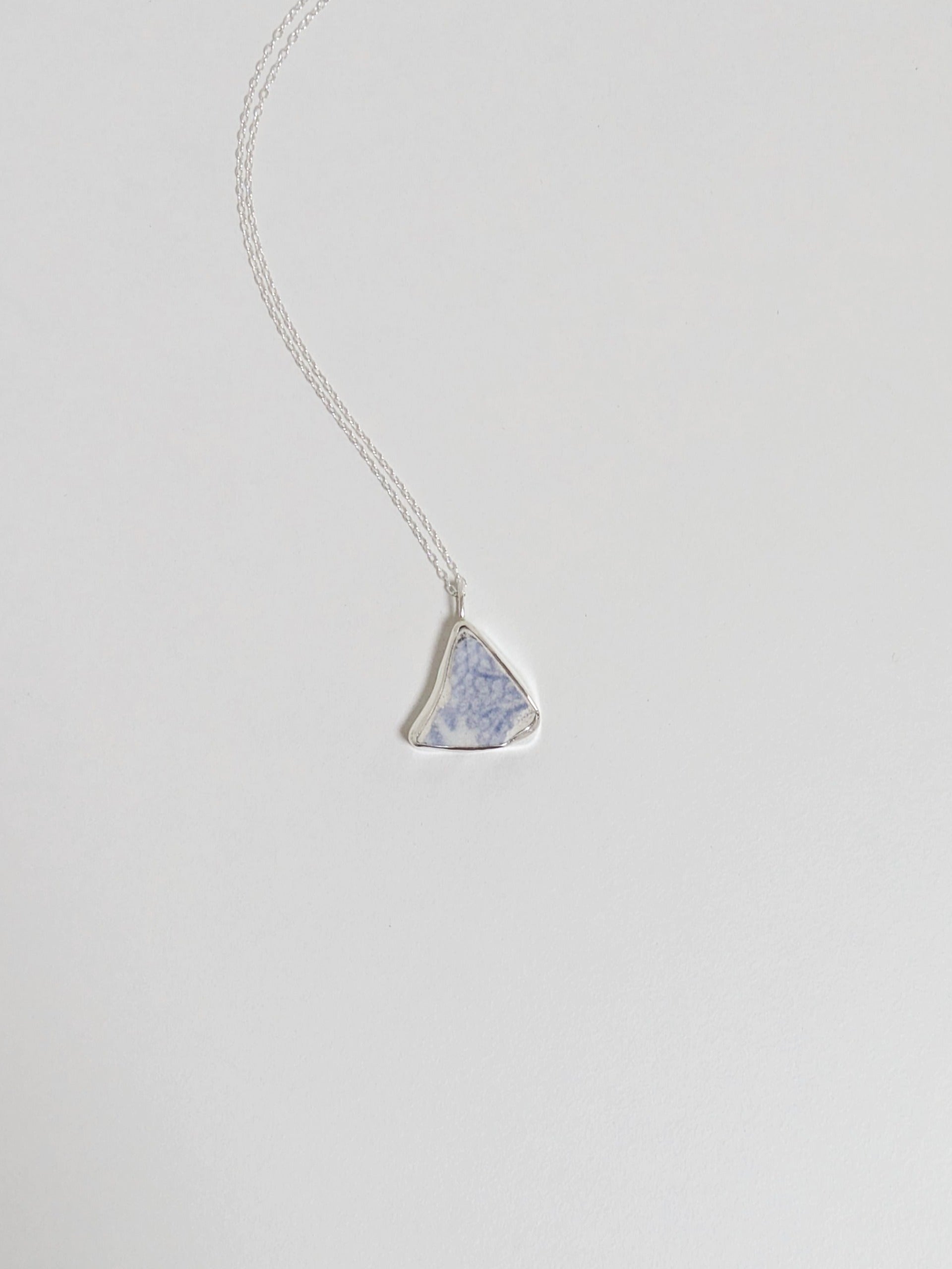 Silver necklace with a triangular blue floral sea pottery pendant on a light gray background