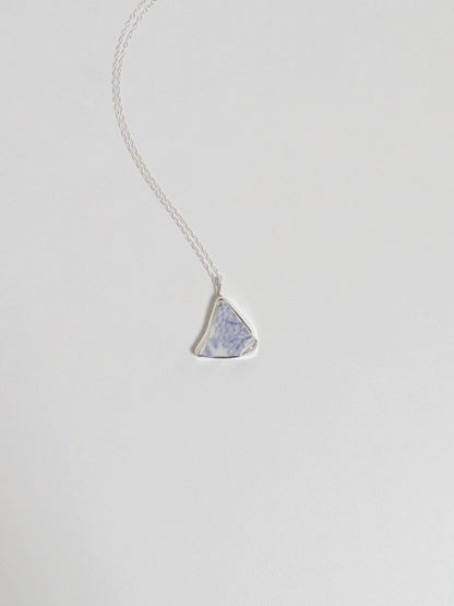 Silver necklace with a triangular blue floral sea pottery pendant on a light gray background
