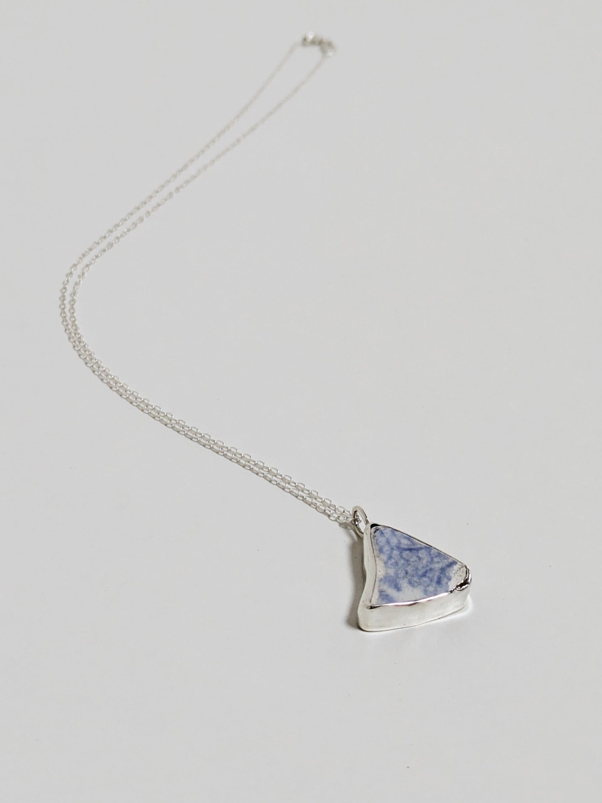 Triangular blue floral sea pottery necklace laying on a white background