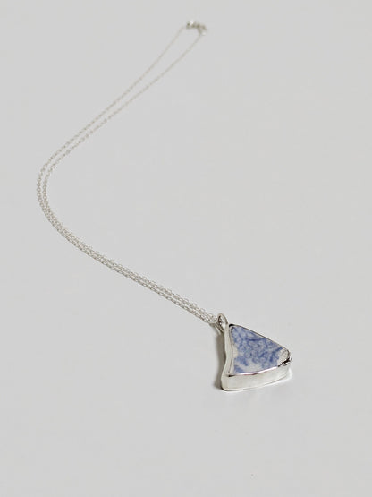 Triangular blue floral sea pottery necklace laying on a white background