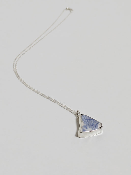 Triangular blue floral sea pottery necklace laying on a white background