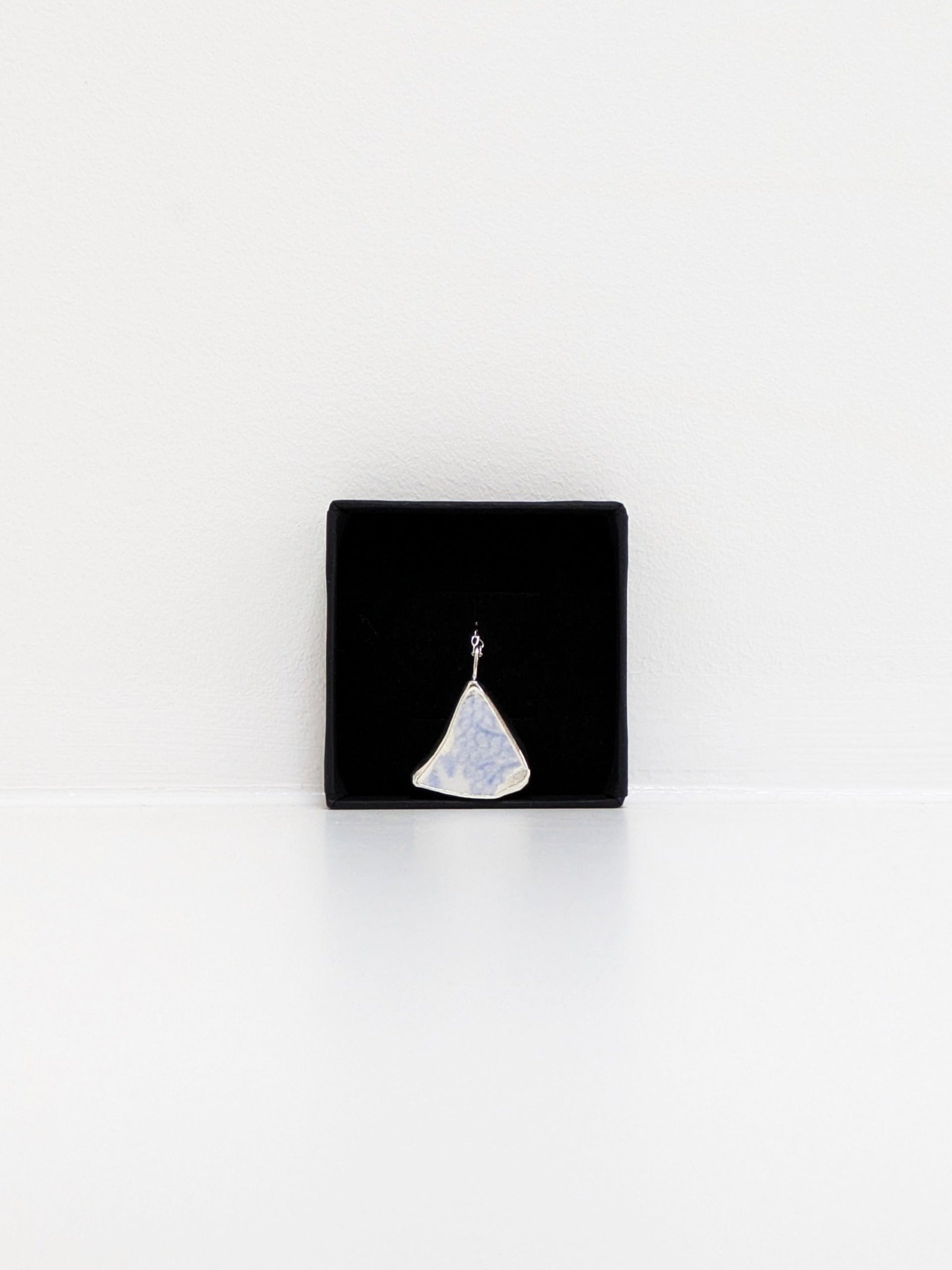Black jewellery display box with a blue floral sea pottery pendant on a white background