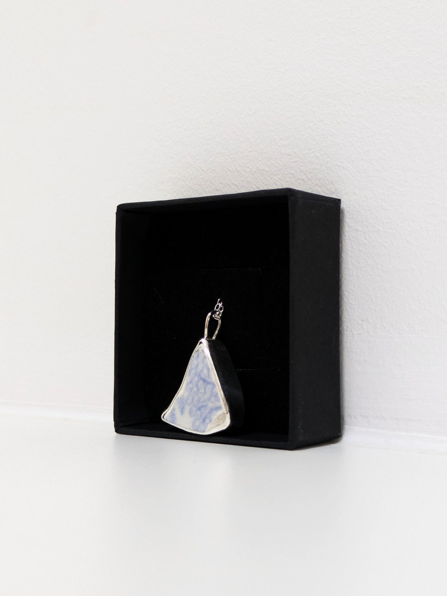 Close up of a blue floral sea pottery pendant  in a jewellery box on a white background