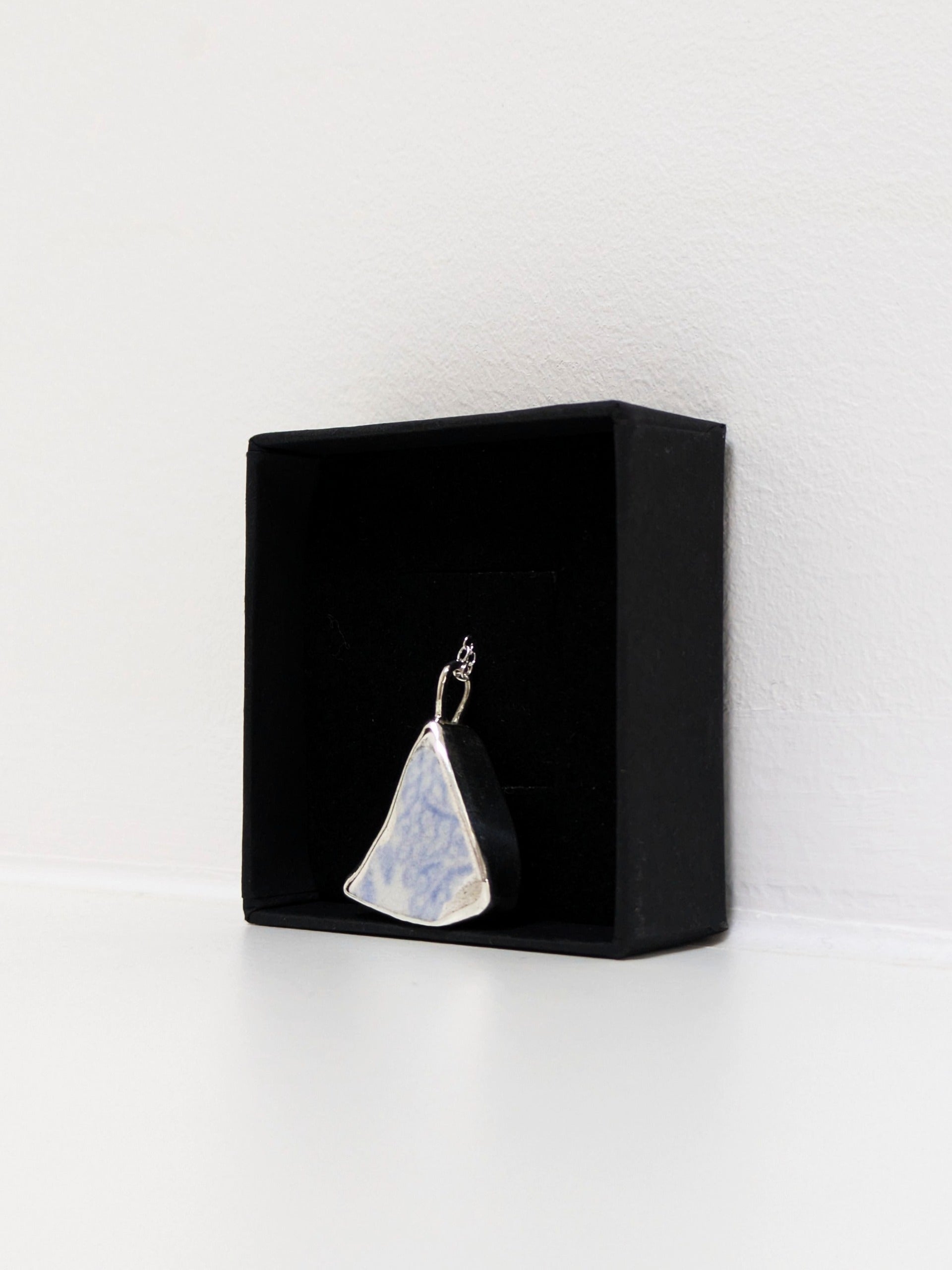 Close up of a blue floral sea pottery pendant  in a jewellery box on a white background