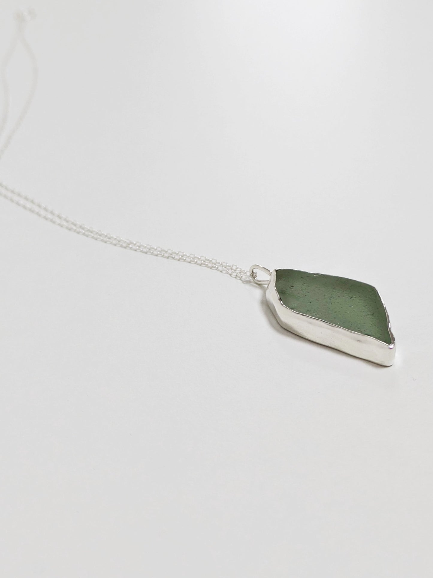Side profile of a big turquoise sea glass pendant with a silver chain on a white background.
