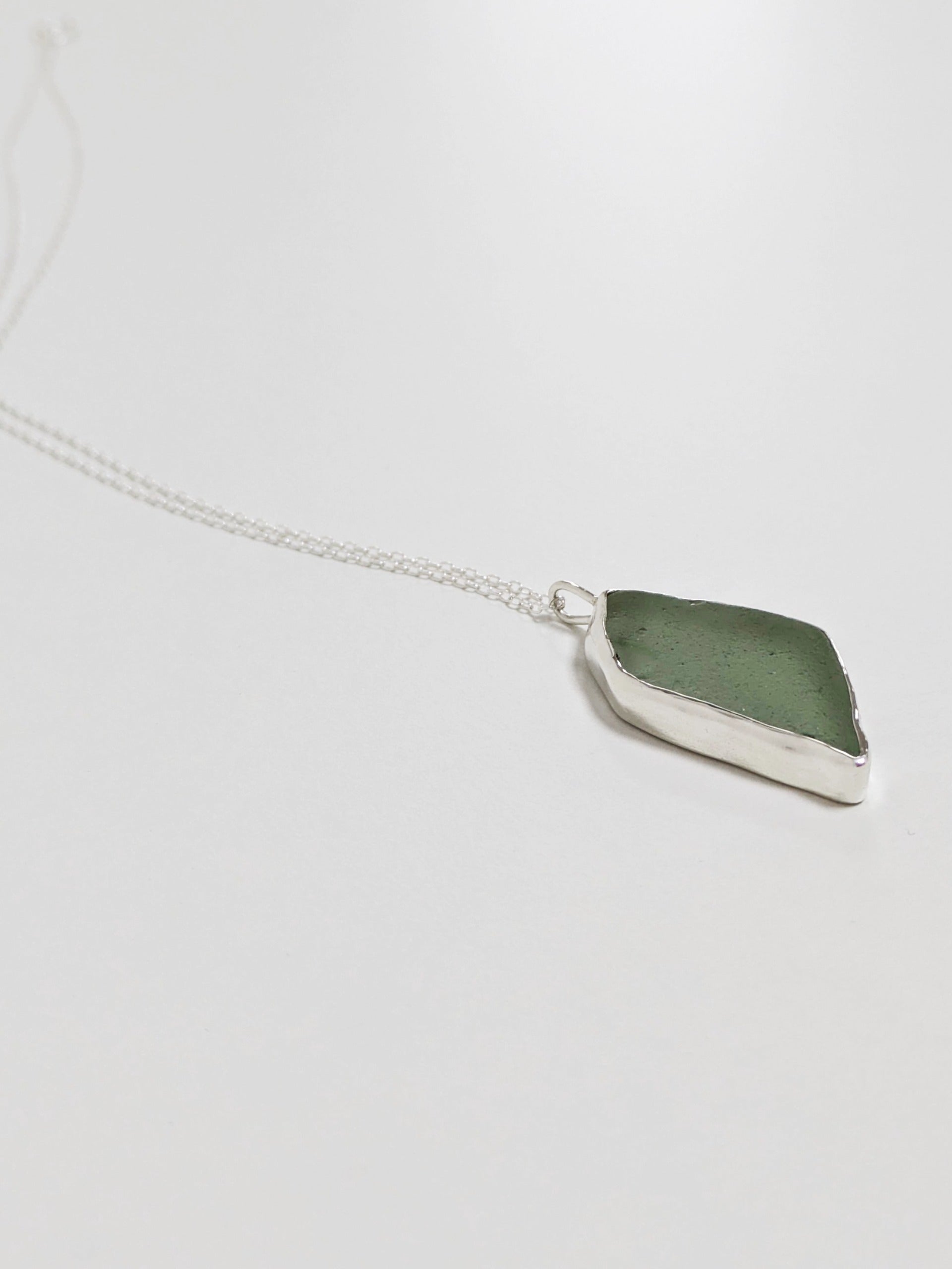 Side profile of a big turquoise sea glass pendant with a silver chain on a white background.
