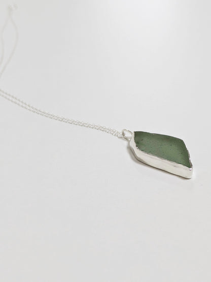 Side profile of a big turquoise sea glass pendant with a silver chain on a white background.