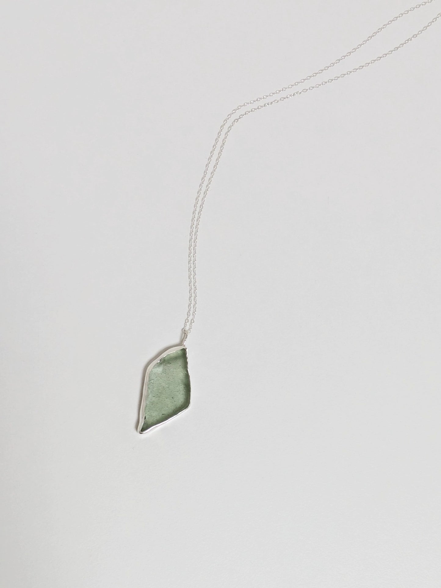 Picture of a big turquoise sea glass pendant at an angle with a silver chain on a white background.