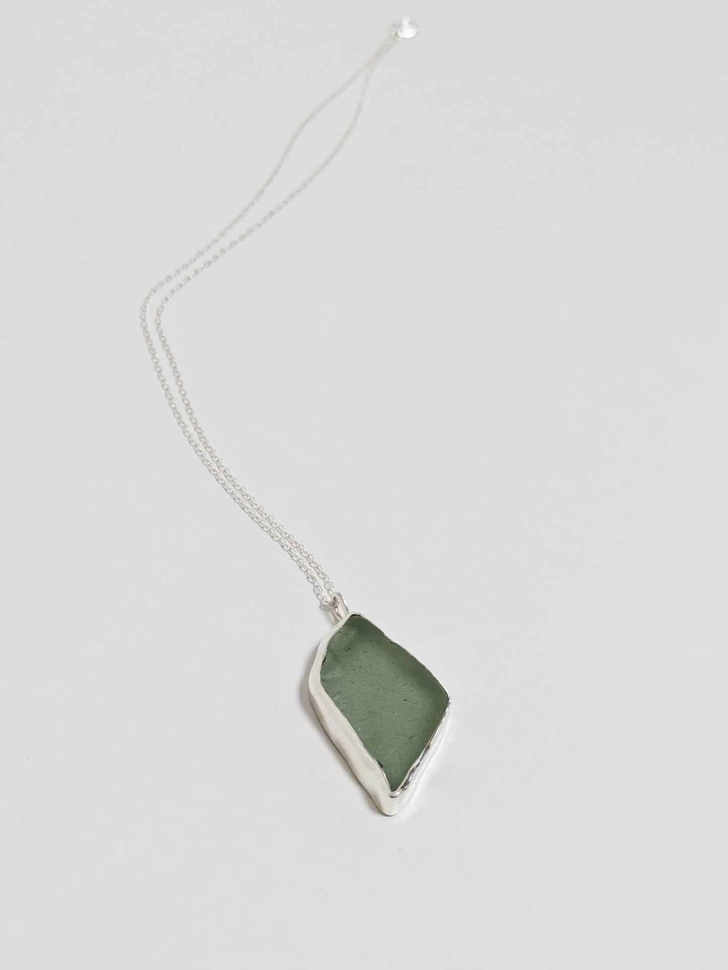 Close up of a big turquoise sea glass pendant with a silver chain on a white background.
